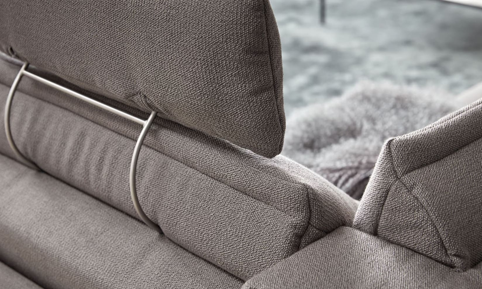 Nahaufnahme des Himolla Sofa Spektra 1175, ein modernes graues Stoffsofa mit verstellbaren Kopfstützen und Metallstützen, im Hintergrund ist ein Teppich zu sehen. Nahaufnahme des Himolla Sofa Spektra 1175, ein modernes graues Stoffsofa mit verstellbaren Kopfstützen und Metallstützen, im Hintergrund ist ein Teppich zu sehen.