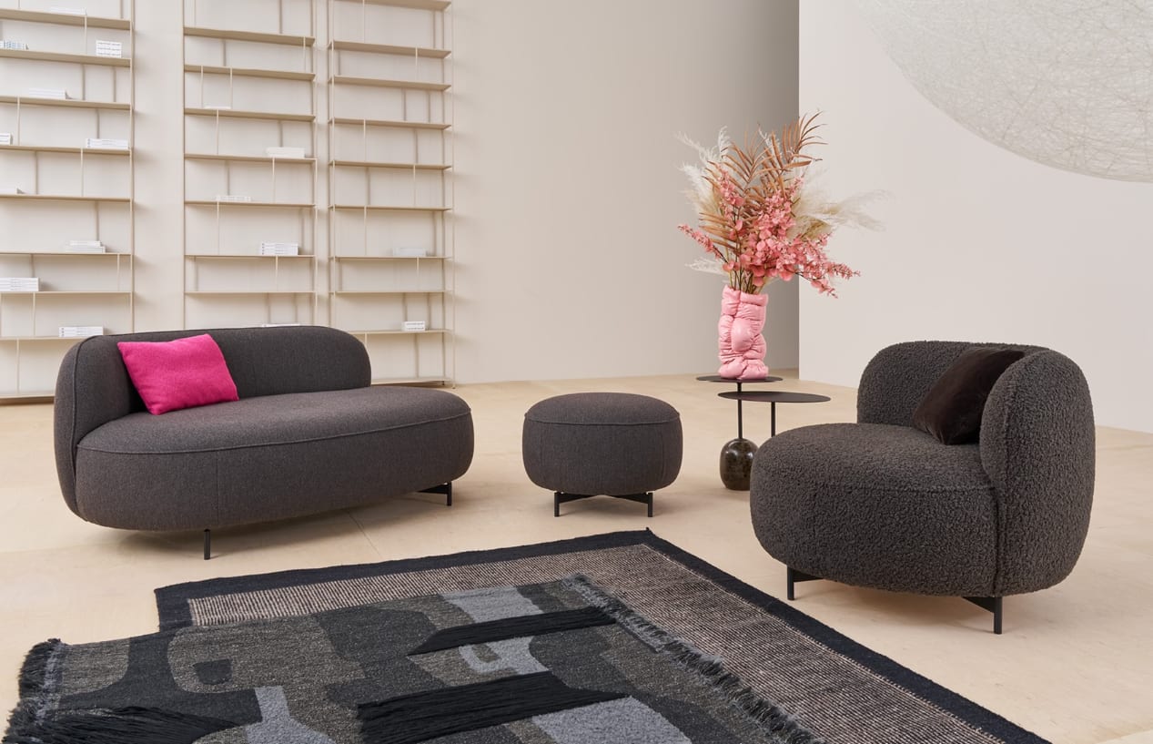 Modernes Wohnzimmer mit dem Himolla Einzelsessel 7596, dunkelgrauem Sofa, Ottomane, rosa Kissen und einer Blumenvase auf einem runden Tisch. Modernes Wohnzimmer mit dem Himolla Einzelsessel 7596, dunkelgrauem Sofa, Ottomane, rosa Kissen und einer Blumenvase auf einem runden Tisch.