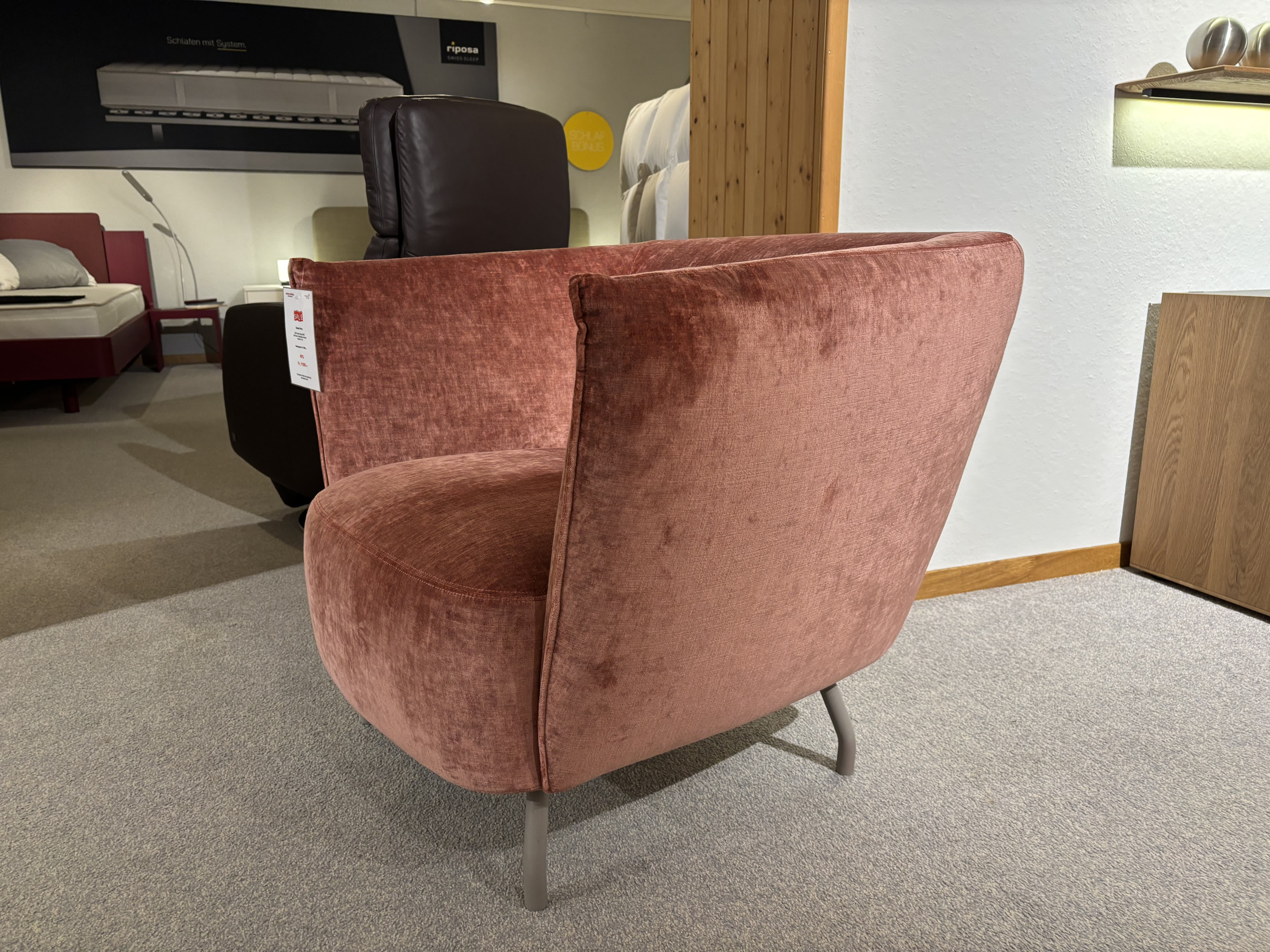 Sur une moquette grise, dans une salle d'exposition où se trouvent des lits et une chaise marron, le fauteuil en velours rose placé à côté du mobilier de bureau avec ses trois caissons et sa fenêtre ajoute une touche d'élégance. Sur une moquette grise, dans une salle d'exposition où se trouvent des lits et une chaise marron, le fauteuil en velours rose placé à côté du mobilier de bureau avec ses trois caissons et sa fenêtre ajoute une touche d'élégance.