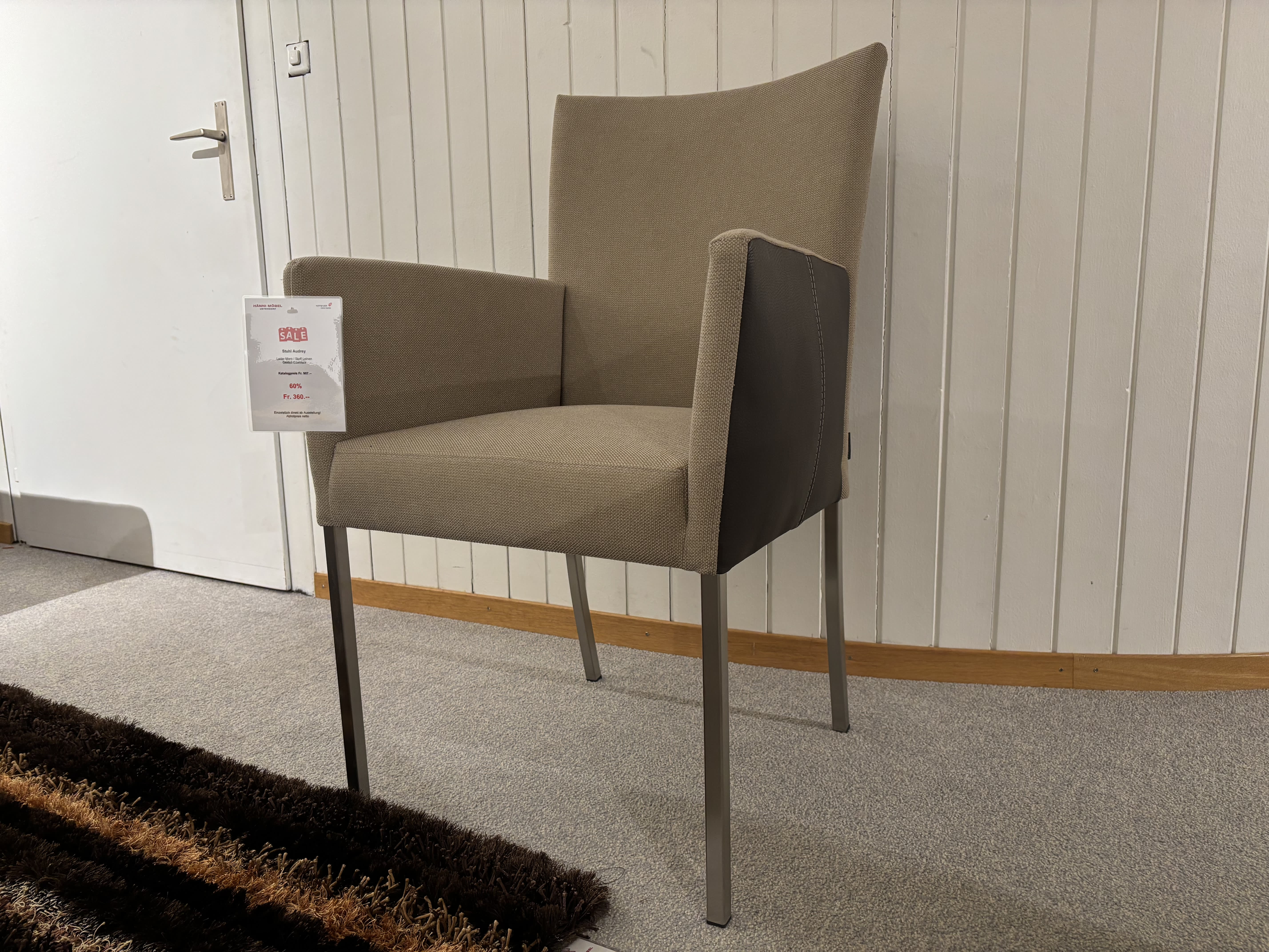 Ein grauer Stoffsessel mit Metallrahmen von Büromöbel mit 3 Boxen Window steht neben einer weißen Tür auf einem grauen Teppich, begleitet von einem braun gestreiften Läufer. Ein grauer Stoffsessel mit Metallrahmen von Büromöbel mit 3 Boxen Window steht neben einer weißen Tür auf einem grauen Teppich, begleitet von einem braun gestreiften Läufer.