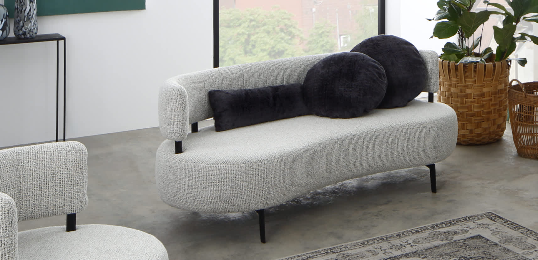In einem hellen Raum mit großen Fenstern verfügt das Ponsel Sofa Organic in modernem Grau über schwarze runde und zylindrische Kissen, ergänzt durch einen Pflanzenkorb. In einem hellen Raum mit großen Fenstern verfügt das Ponsel Sofa Organic in modernem Grau über schwarze runde und zylindrische Kissen, ergänzt durch einen Pflanzenkorb.