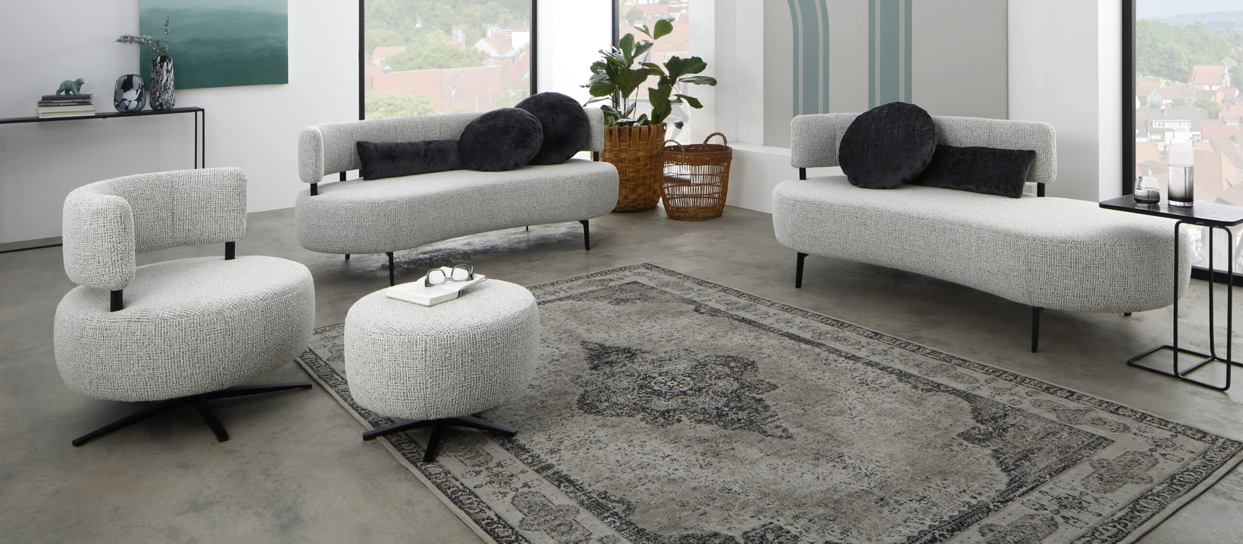 Modernes Wohnzimmer mit Ponsel Sofa Organic, rundem Ottoman und dekorativem Teppich. Große Fenster und Zimmerpflanzen sorgen für Helligkeit. Modernes Wohnzimmer mit Ponsel Sofa Organic, rundem Ottoman und dekorativem Teppich. Große Fenster und Zimmerpflanzen sorgen für Helligkeit.