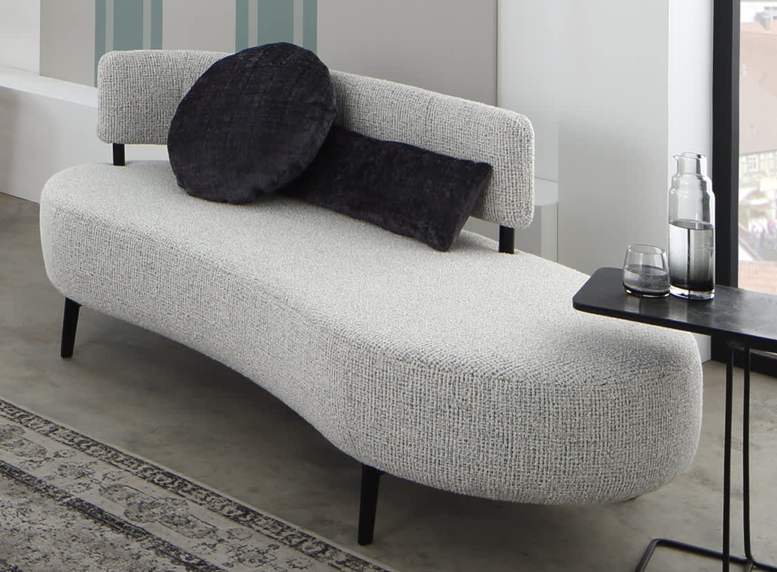 Ein geschwungenes graues Sofa von Ponsel Recamiere Organic mit zwei dunklen, runden Kissen steht neben einem schwarzen Beistelltisch, auf dem eine Glaskanne und ein Glas stehen. Ein geschwungenes graues Sofa von Ponsel Recamiere Organic mit zwei dunklen, runden Kissen steht neben einem schwarzen Beistelltisch, auf dem eine Glaskanne und ein Glas stehen.