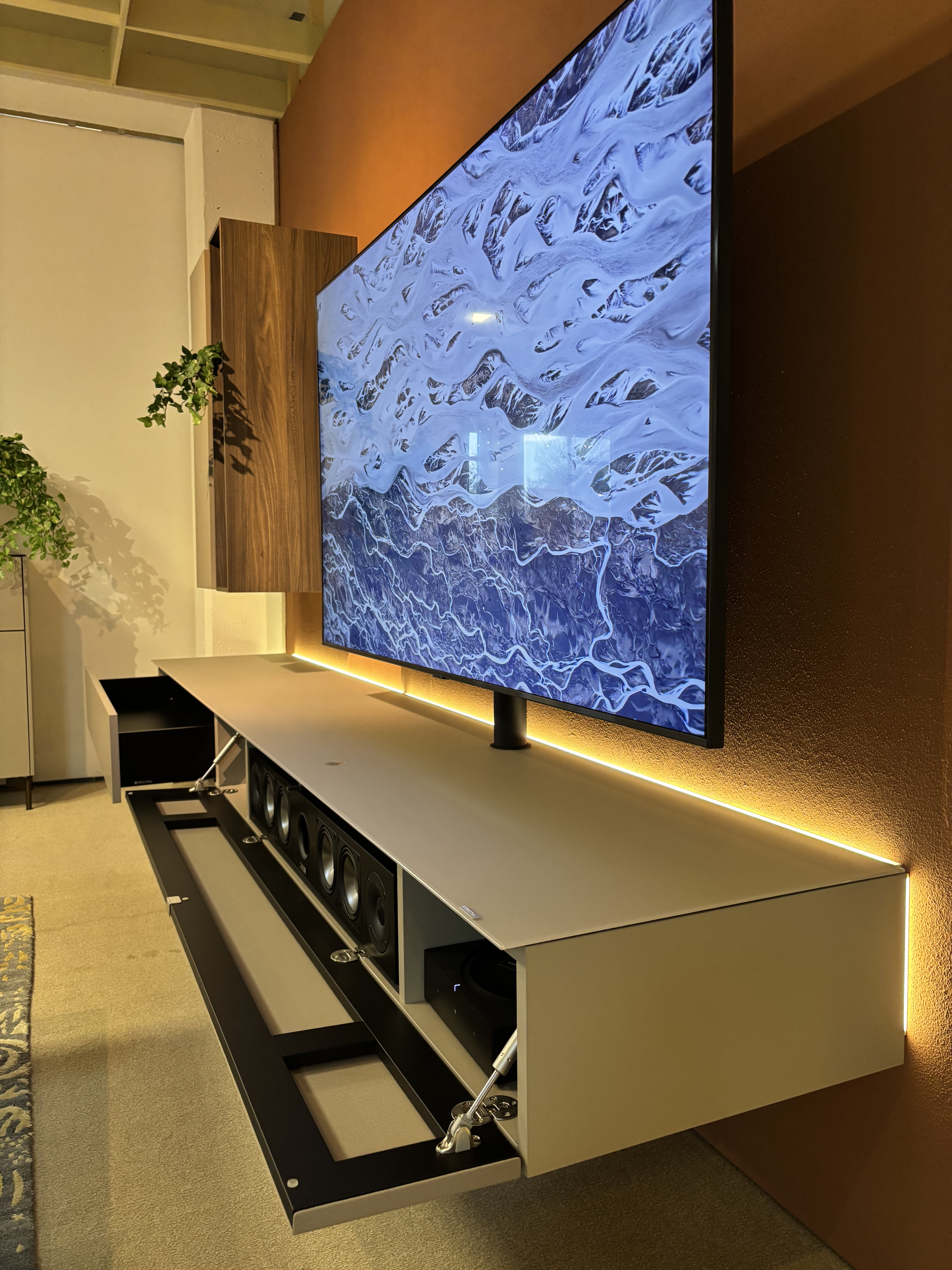 Ein wandmontierter Fernseher über dem Spectral TV-Möbel Next mit offener Front, sichtbaren Lautsprechern im Inneren und warmer LED-Beleuchtung. Ein wandmontierter Fernseher über dem Spectral TV-Möbel Next mit offener Front, sichtbaren Lautsprechern im Inneren und warmer LED-Beleuchtung.
