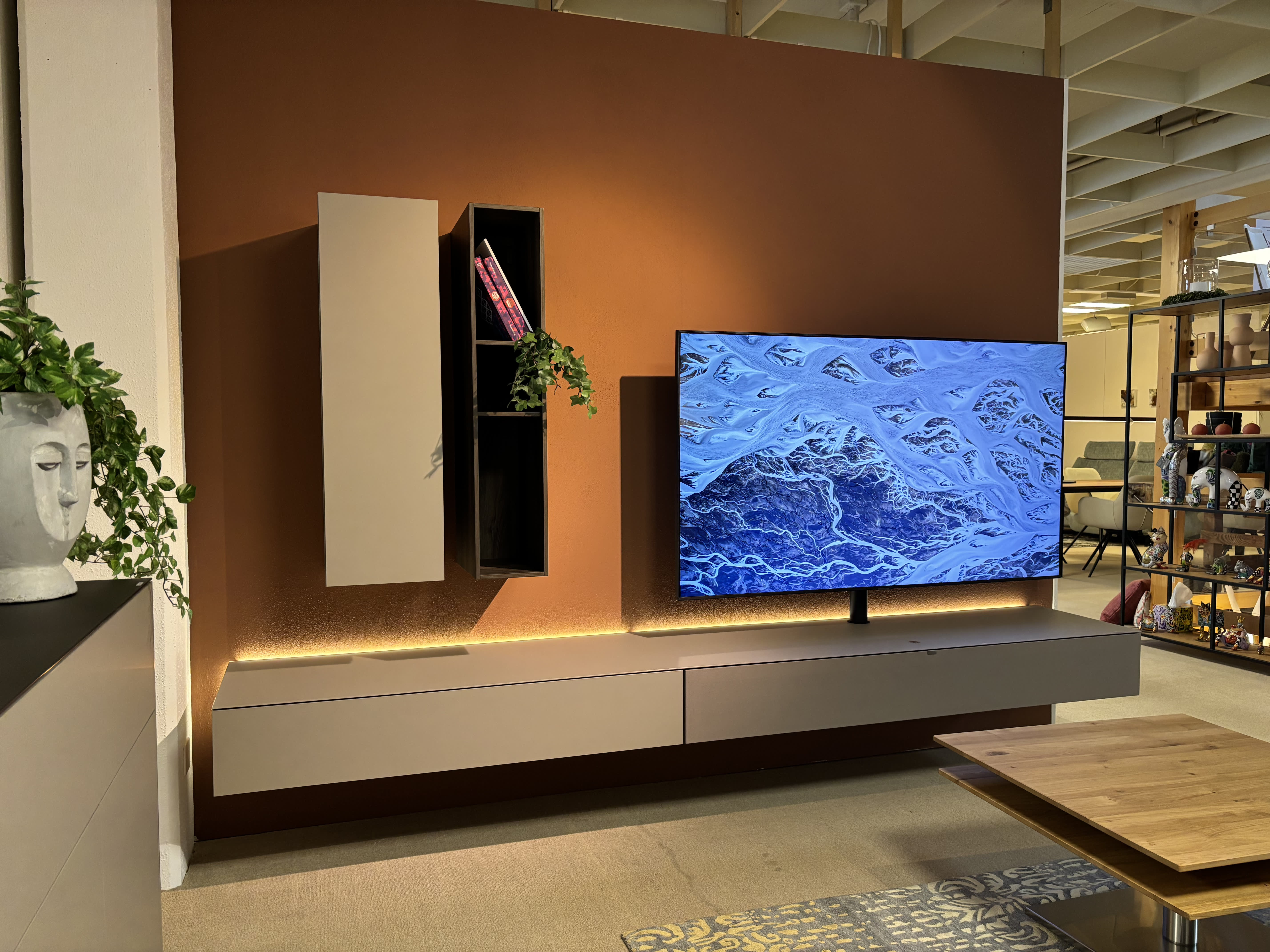 Modernes Wohnzimmer mit dem Spectral TV-Möbel Next Wandgerät, Regalen, Pflanzen und dekorativen Akzenten vor einer braunen Akzentwand. Modernes Wohnzimmer mit dem Spectral TV-Möbel Next Wandgerät, Regalen, Pflanzen und dekorativen Akzenten vor einer braunen Akzentwand.