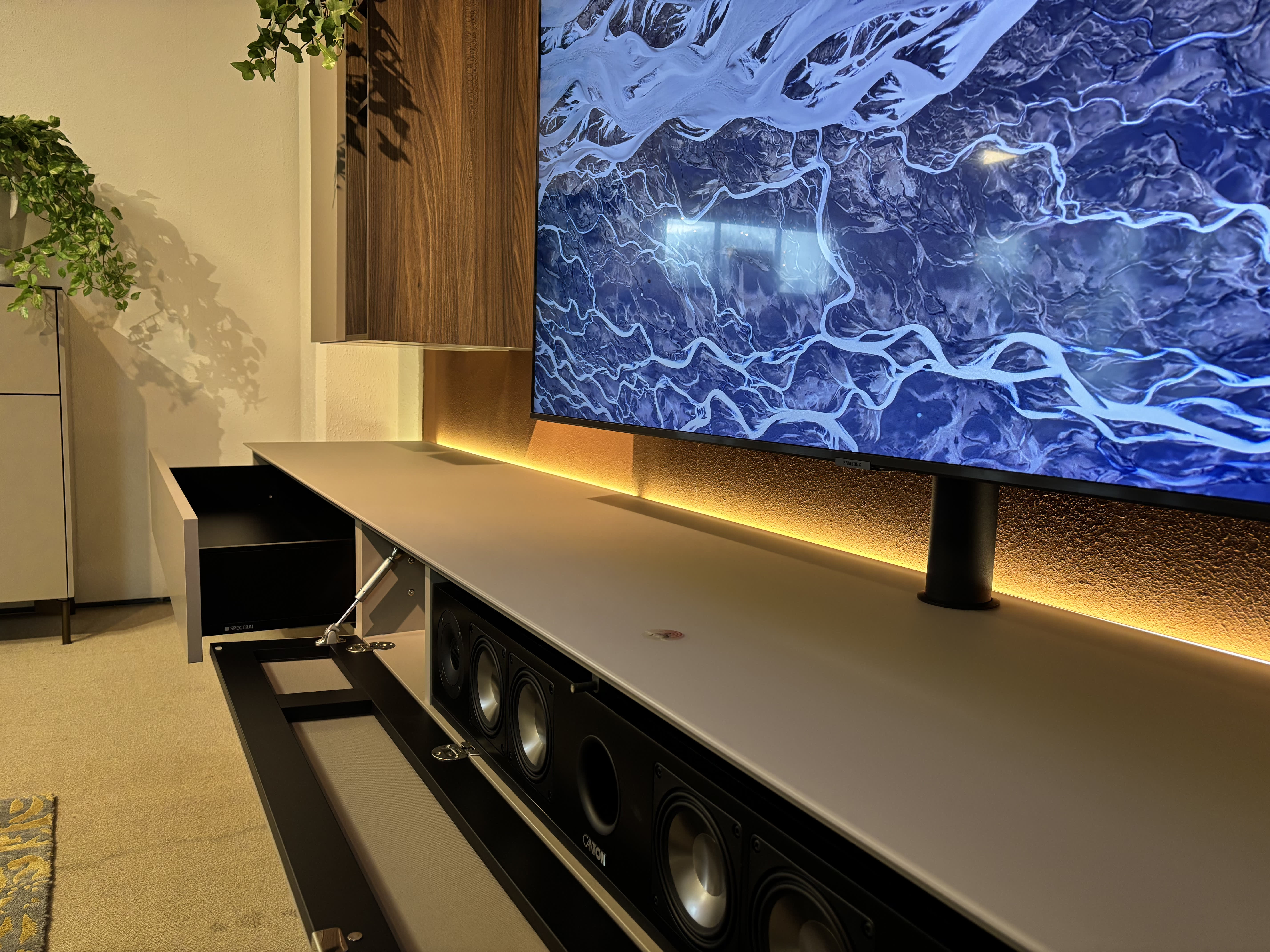 Ein Fernseher an der Wand mit LED-Hintergrundbeleuchtung, gepaart mit einer Soundbar im offenen Gehäuse des TV-Möbels Next von Spectral unten. Ein Fernseher an der Wand mit LED-Hintergrundbeleuchtung, gepaart mit einer Soundbar im offenen Gehäuse des TV-Möbels Next von Spectral unten.