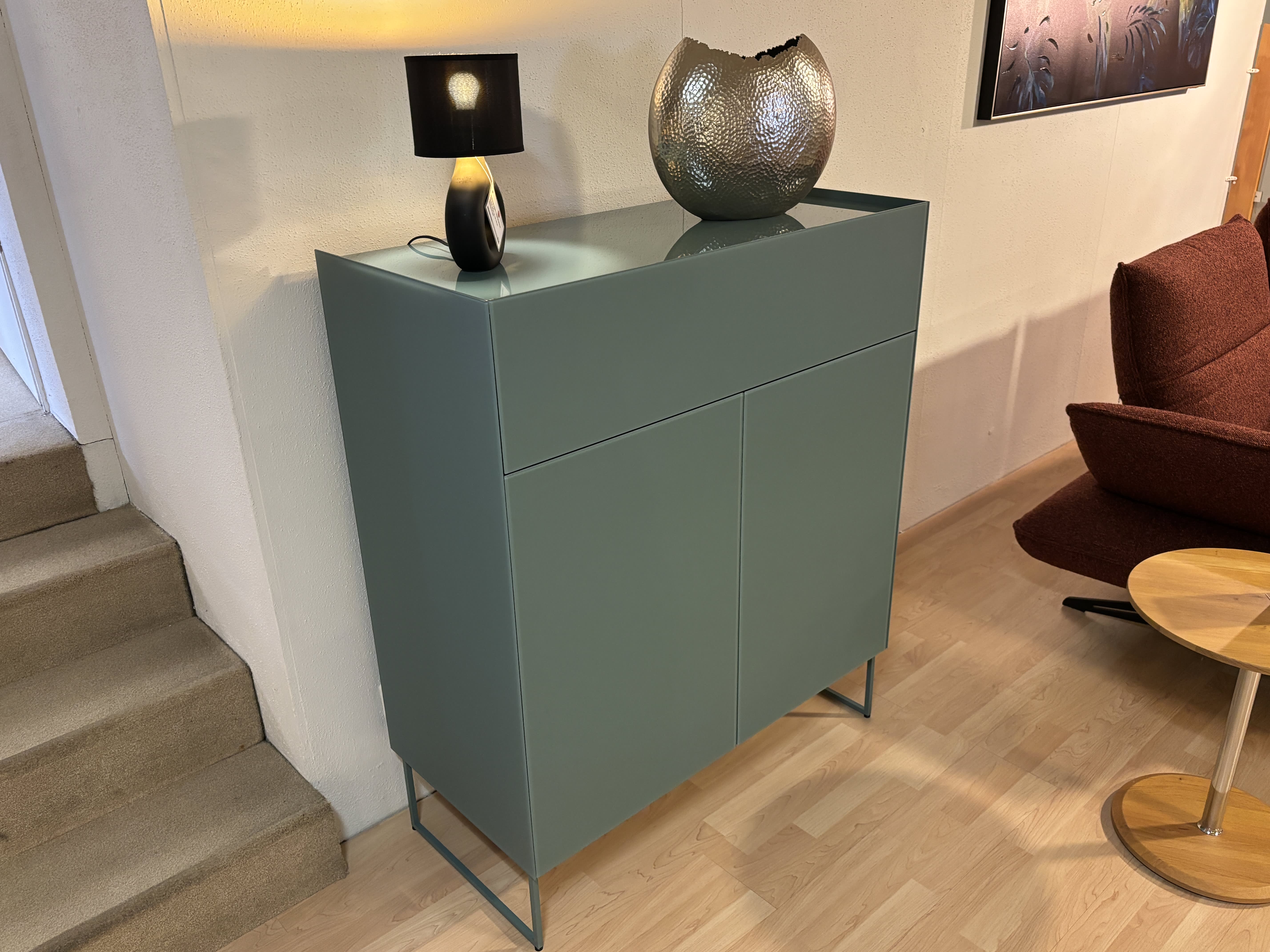 Das Spectral Sideboard 101cm, in grün, ist mit einer Lampe und einer dekorativen Schale auf der Oberseite gestaltet, neben der Treppe platziert und mit einem roten Stuhl kombiniert. Das Spectral Sideboard 101cm, in grün, ist mit einer Lampe und einer dekorativen Schale auf der Oberseite gestaltet, neben der Treppe platziert und mit einem roten Stuhl kombiniert.