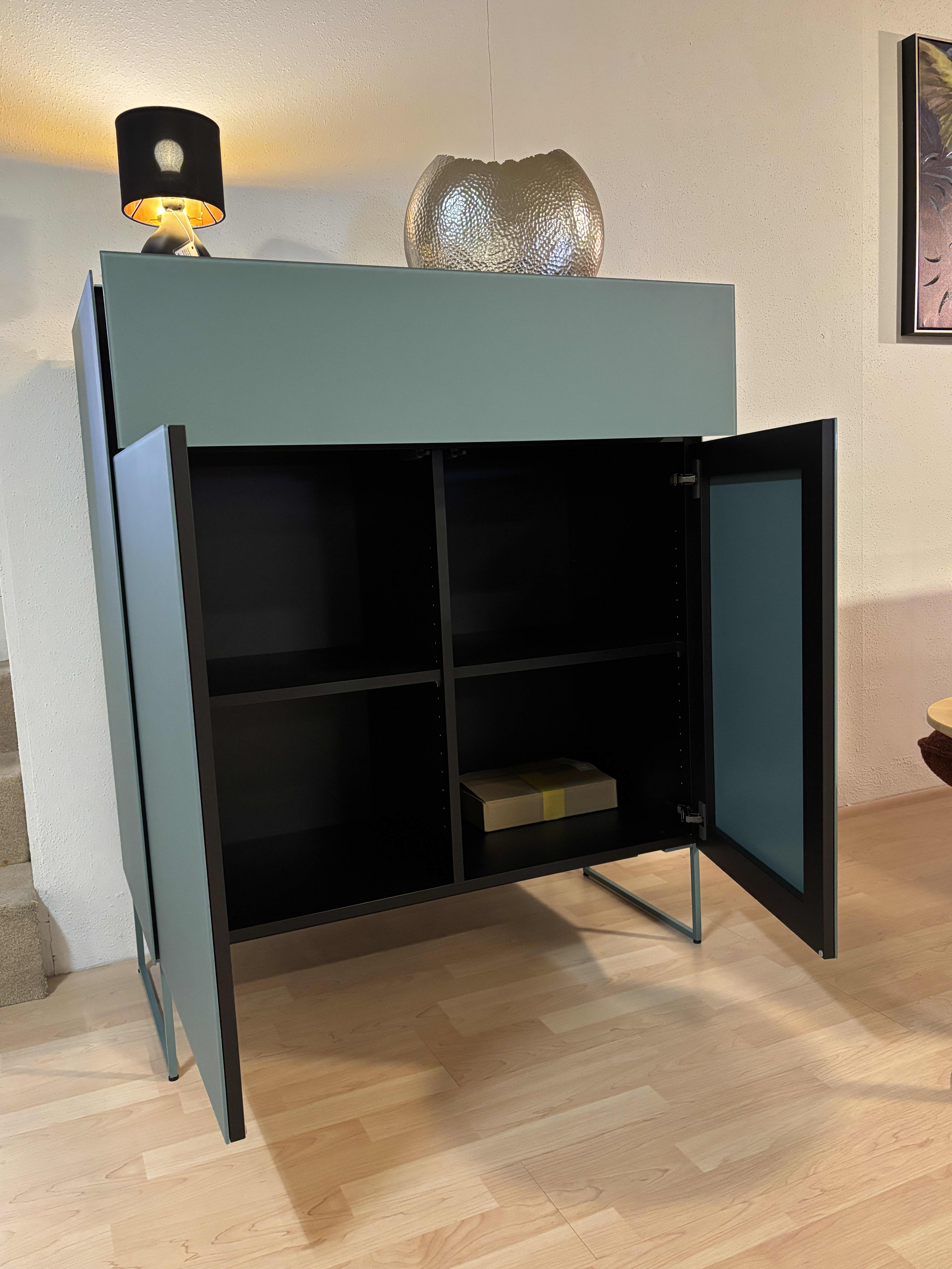Das Spectral Sideboard 101cm ist ein tealfarbener Schrank mit offenen Türen, Einlegeböden und einer Box im Inneren, die mit einer Lampe und einer Glasschale gekrönt wird. Das Spectral Sideboard 101cm ist ein tealfarbener Schrank mit offenen Türen, Einlegeböden und einer Box im Inneren, die mit einer Lampe und einer Glasschale gekrönt wird.