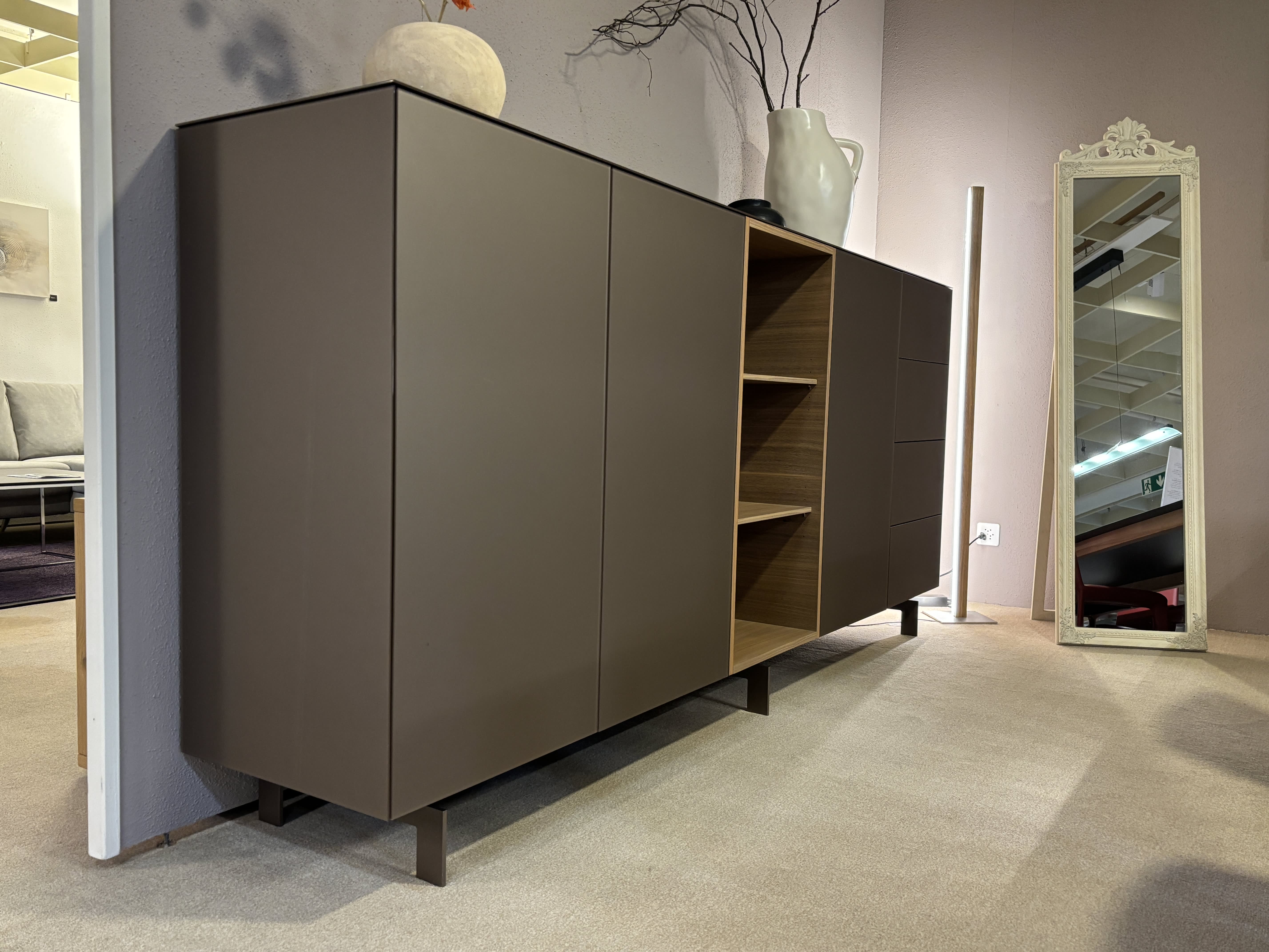 Das Spectral Sideboard 250cm verfügt über offene Regale, eine dekorative Vase auf der Oberseite und wird mit einem hohen Spiegel im Wohnbereich kombiniert. Das Spectral Sideboard 250cm verfügt über offene Regale, eine dekorative Vase auf der Oberseite und wird mit einem hohen Spiegel im Wohnbereich kombiniert.