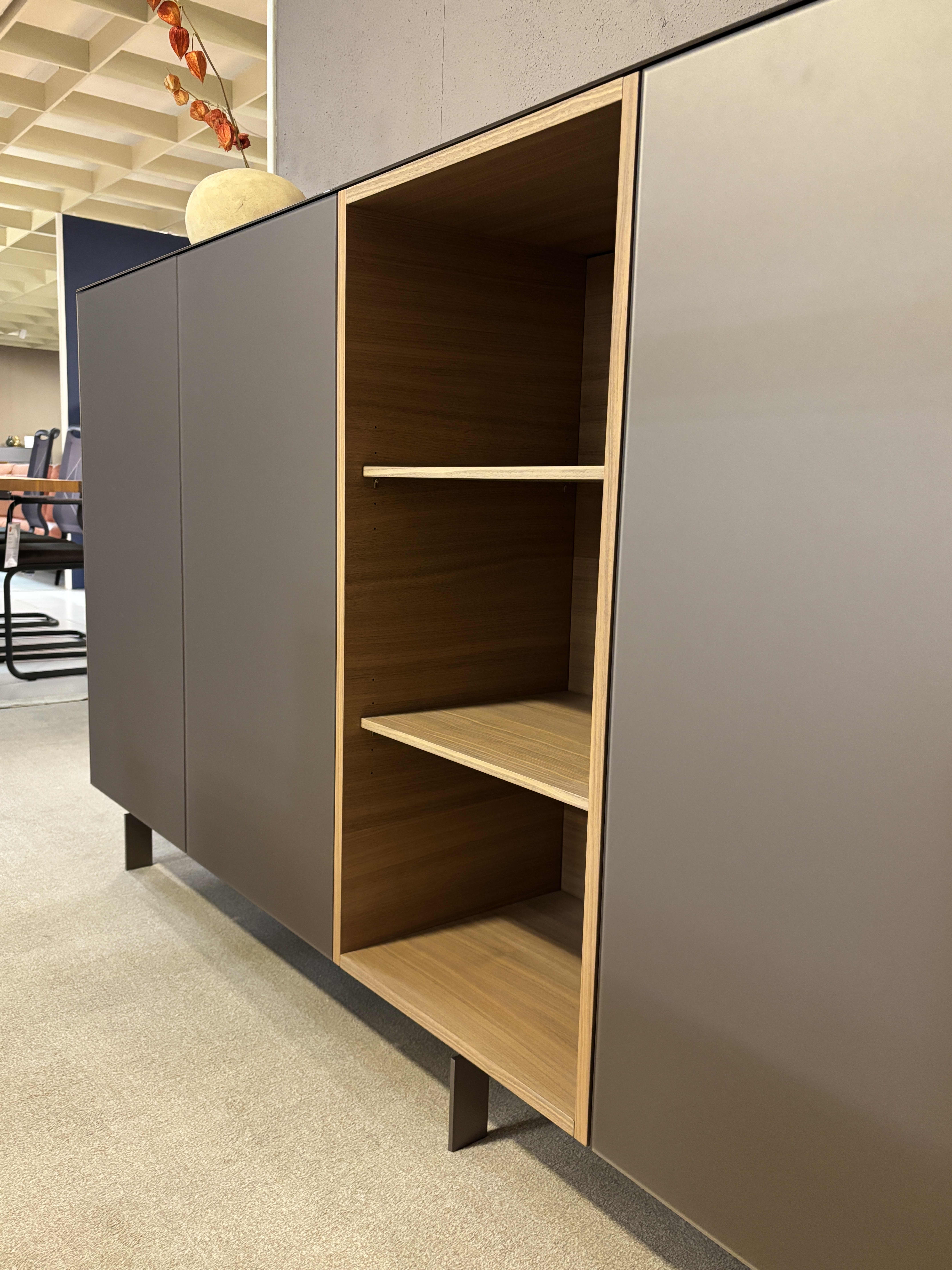 Das Spectral Sideboard 250cm hat matte, dunkle Türen, ein offenes Holzregal und Metallbeine, die jedem Büro einen modernen Touch verleihen. Das Spectral Sideboard 250cm hat matte, dunkle Türen, ein offenes Holzregal und Metallbeine, die jedem Büro einen modernen Touch verleihen.