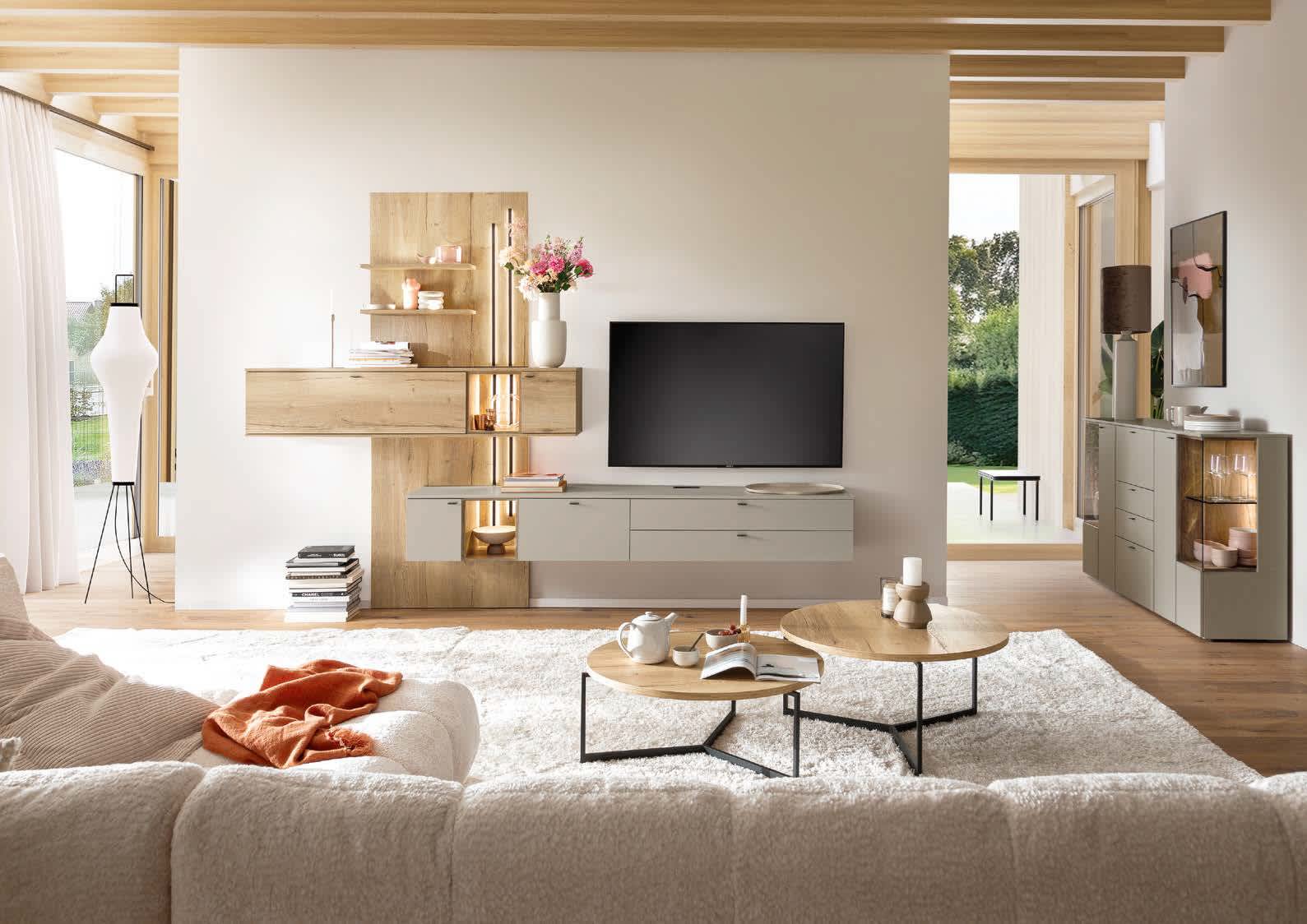 Das Venjakob Wohnprogramm Vanya bietet eine moderne Wohnzimmereinrichtung mit neutralen Tönen, einem großen Fernseher, Holzregalen und einem gemütlichen beigen Sofa, das durch einen stilvollen Teppich ergänzt wird. Das Venjakob Wohnprogramm Vanya bietet eine moderne Wohnzimmereinrichtung mit neutralen Tönen, einem großen Fernseher, Holzregalen und einem gemütlichen beigen Sofa, das durch einen stilvollen Teppich ergänzt wird.