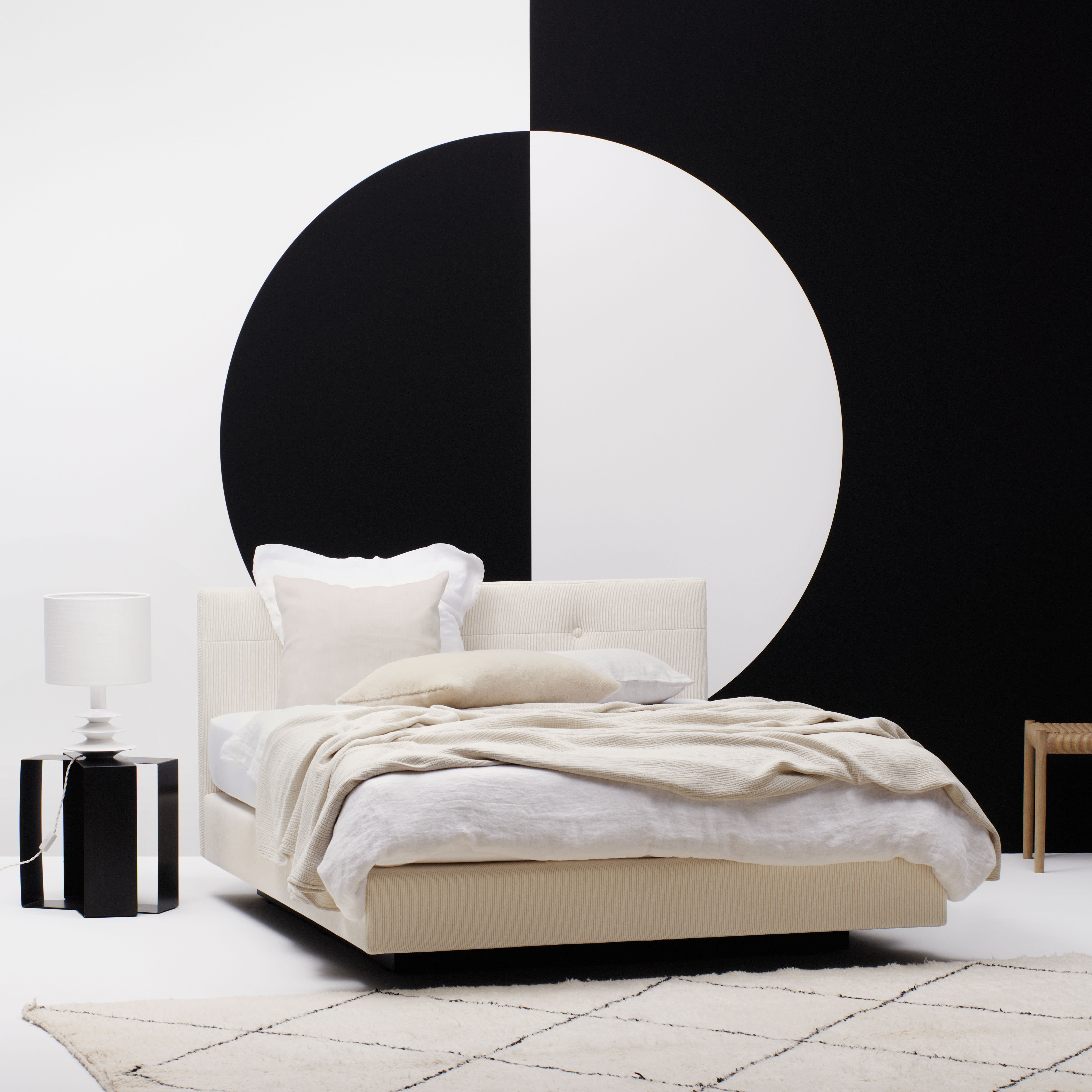 Modernes Schlafzimmer mit dem Riposa Boxspringbett Aurora Relax in Beige mit weißer Bettwäsche, ergänzt durch ein auffälliges Wandbild mit schwarz-weißen Kreisen im Hintergrund.