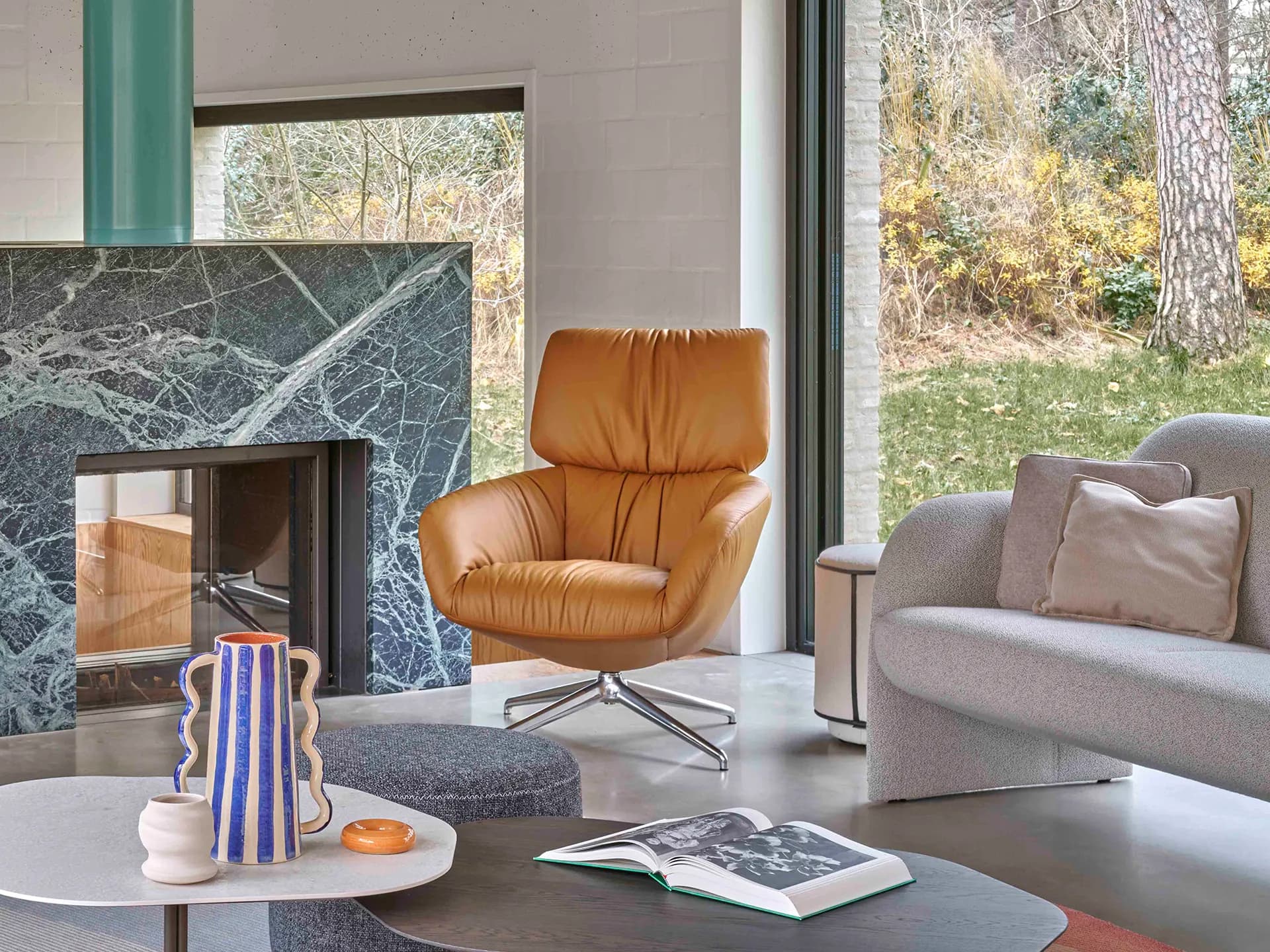 Modernes Wohnzimmer mit dem Leolux Sessel Lodey, grauem Sofa, Marmorkamin und einem Couchtisch mit Büchern und einer Vase. Modernes Wohnzimmer mit dem Leolux Sessel Lodey, grauem Sofa, Marmorkamin und einem Couchtisch mit Büchern und einer Vase.