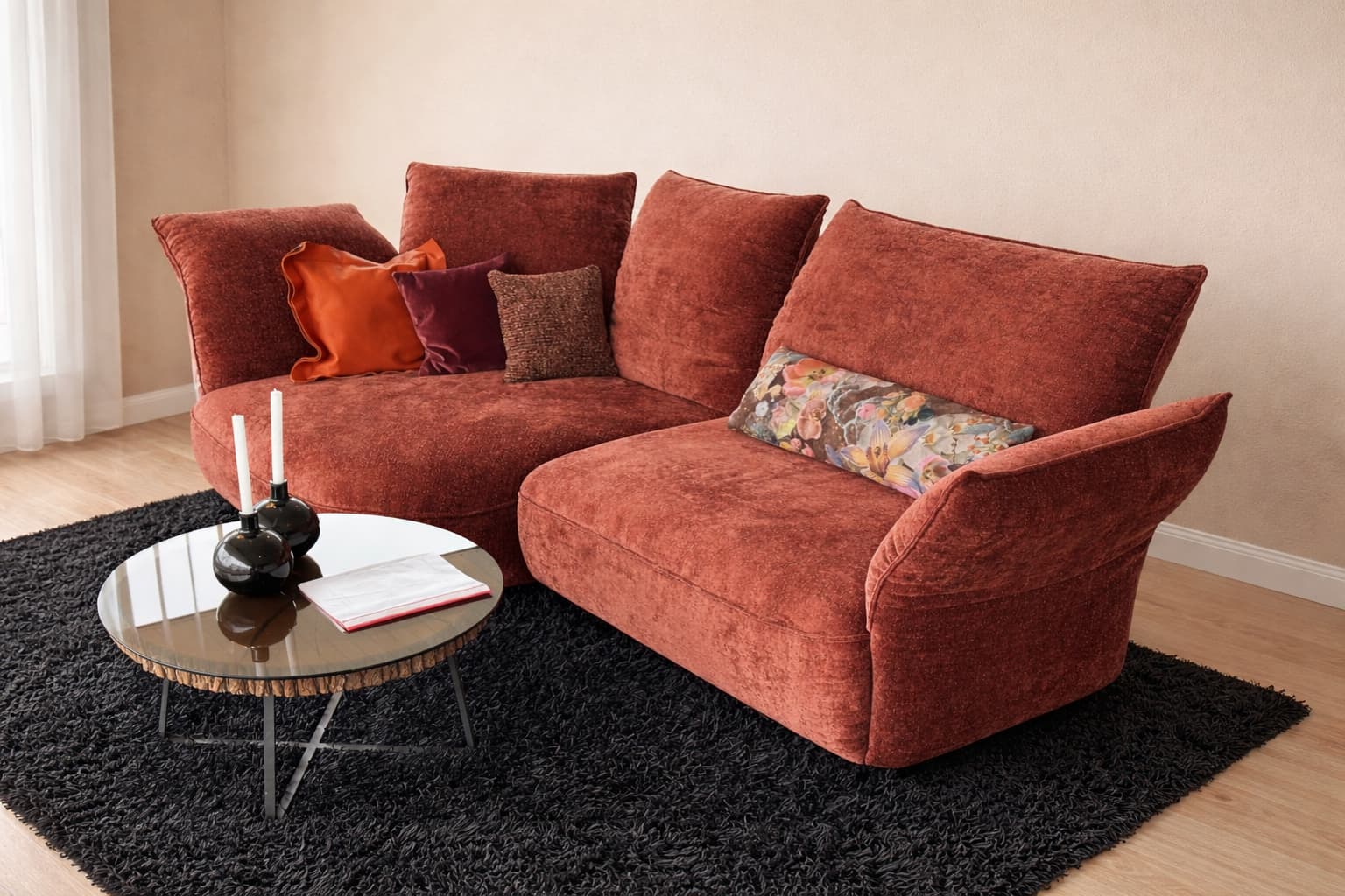 Das rote Samtsofa der Koinor Polstergruppe Abby mit verschiedenen Kissen steht auf einem schwarzen Teppich neben einem runden Couchtisch aus Glas, auf dem Kerzen und ein Buch stehen. Das rote Samtsofa der Koinor Polstergruppe Abby mit verschiedenen Kissen steht auf einem schwarzen Teppich neben einem runden Couchtisch aus Glas, auf dem Kerzen und ein Buch stehen.