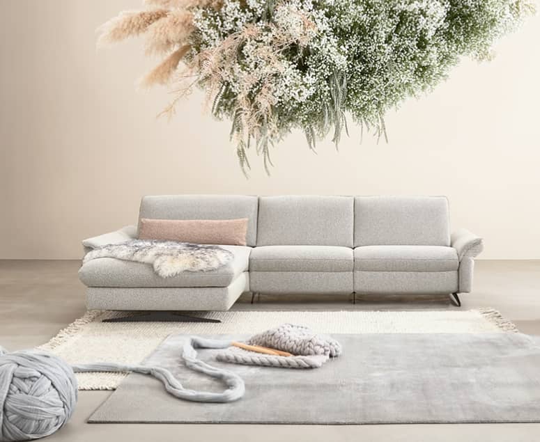 Modernes Wohnzimmer mit dem grauen Sofa Himolla Polstergruppe Spektra 1178, einem weichen Teppich, Akzenten aus Grobstrick und einem hängenden Blumenarrangement darüber. Modernes Wohnzimmer mit dem grauen Sofa Himolla Polstergruppe Spektra 1178, einem weichen Teppich, Akzenten aus Grobstrick und einem hängenden Blumenarrangement darüber.