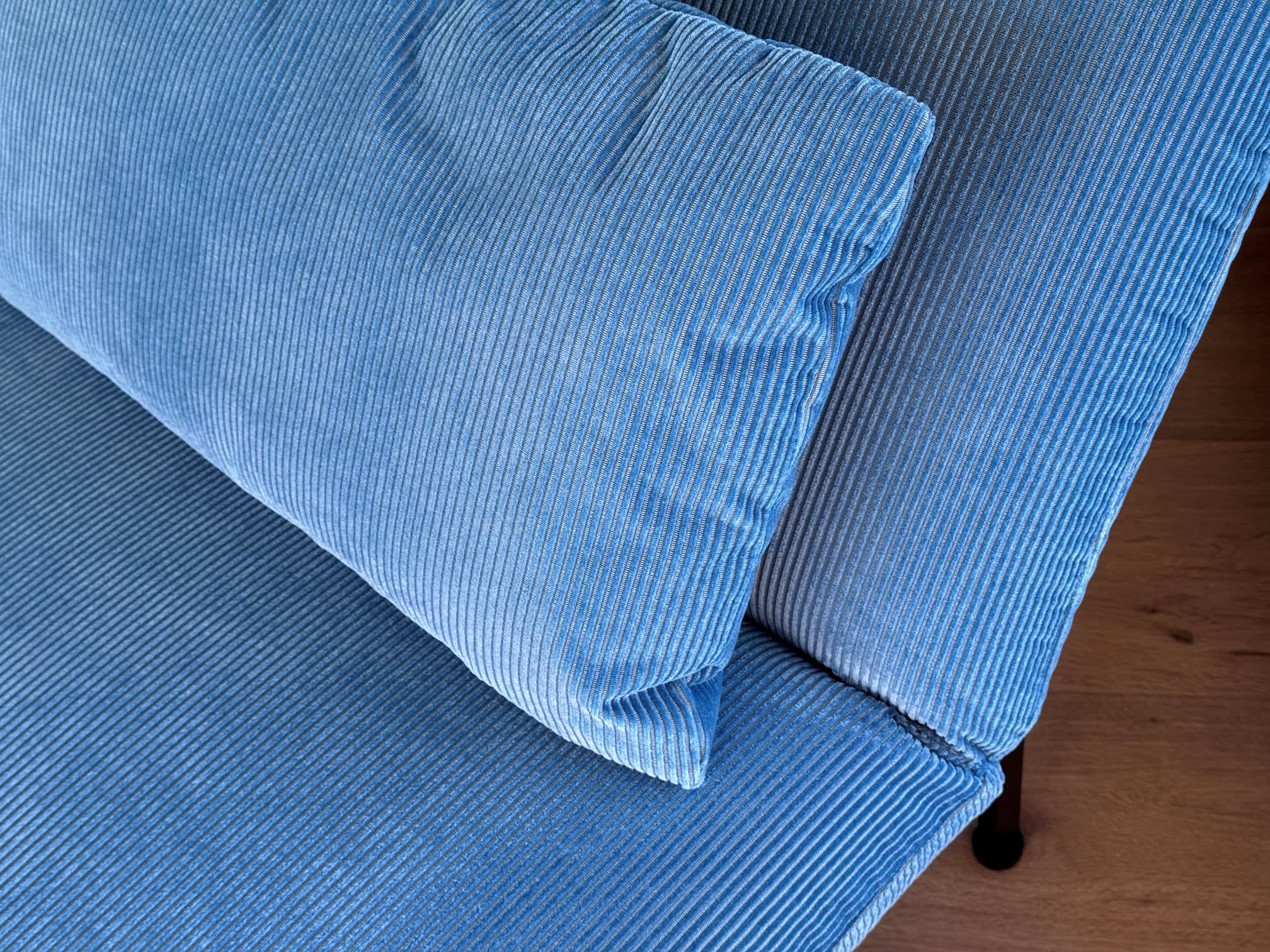 Das blaue Kordkissen Liege Roro 98 liegt auf einem passenden Sofa, im Hintergrund ist ein Holzboden zu sehen. Das blaue Kordkissen Liege Roro 98 liegt auf einem passenden Sofa, im Hintergrund ist ein Holzboden zu sehen.