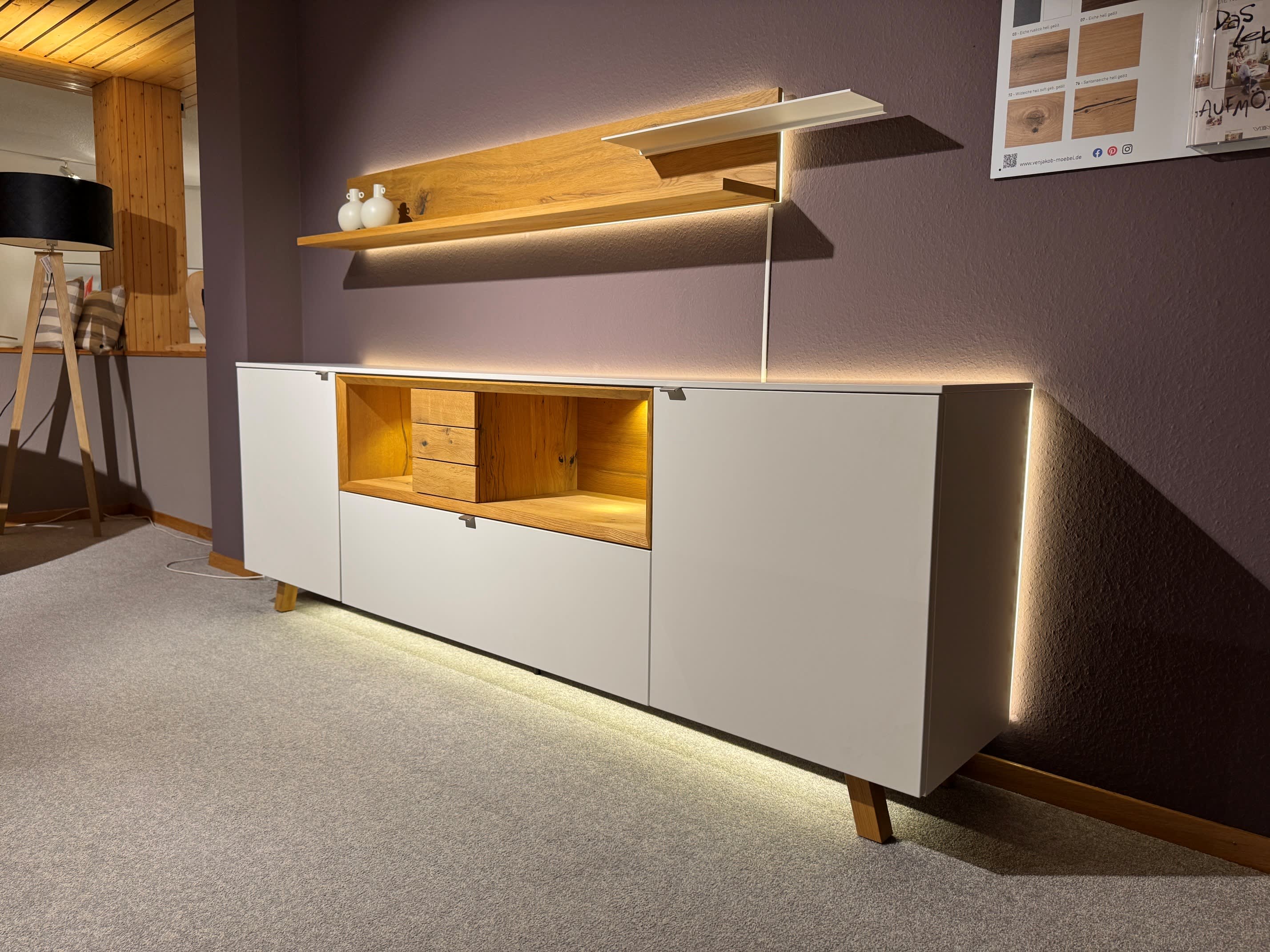 Das Venjakob Wohnprogramm Andiamo Home Sideboard besticht durch sein modernes weißes Design mit Holzakzenten, LED-Beleuchtung und einem an der Wand befestigten Regal, das jeden Raum stilvoll aufwertet. Das Venjakob Wohnprogramm Andiamo Home Sideboard besticht durch sein modernes weißes Design mit Holzakzenten, LED-Beleuchtung und einem an der Wand befestigten Regal, das jeden Raum stilvoll aufwertet.