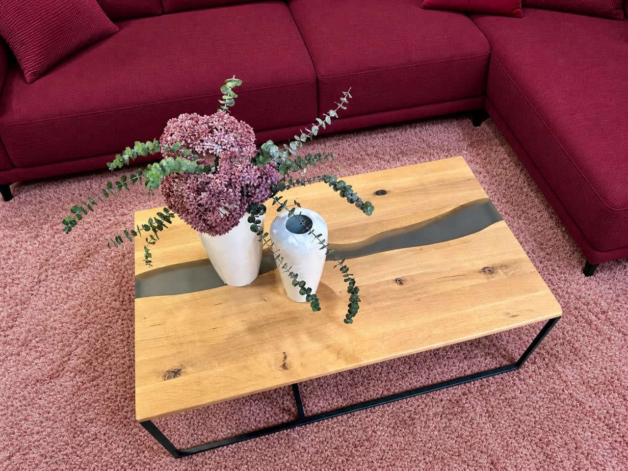 Ein hölzerner Couchtisch mit zwei Vasen, eine davon mit Blumen, auf einem rosa Teppich neben einem roten Sektionssofa. Ein hölzerner Couchtisch mit zwei Vasen, eine davon mit Blumen, auf einem rosa Teppich neben einem roten Sektionssofa.