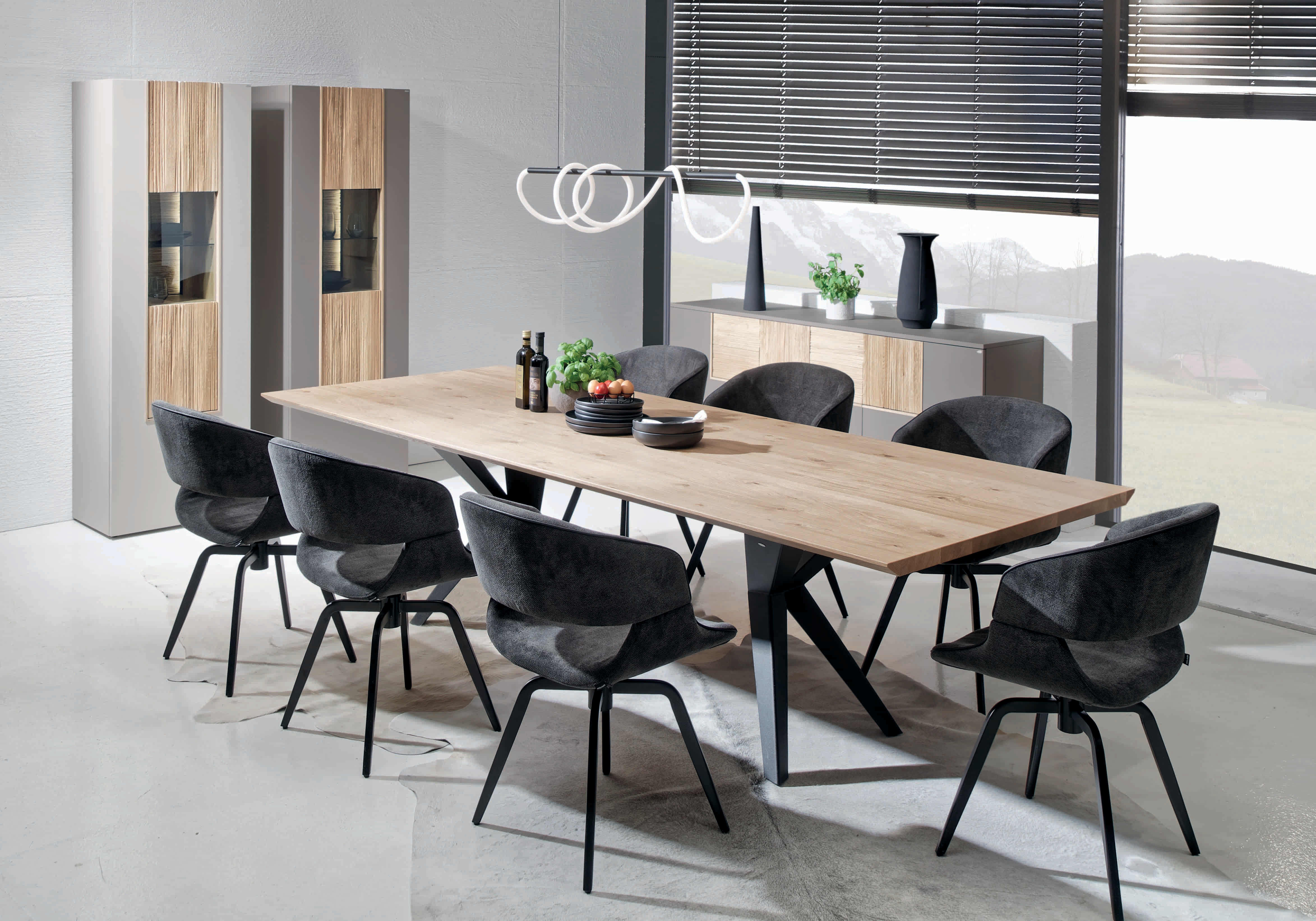 Modernes Esszimmer mit dem Voglauer Lacera Tisch, acht schwarzen Stühlen und minimalistischem Dekor in der Nähe großer Fenster. Modernes Esszimmer mit dem Voglauer Lacera Tisch, acht schwarzen Stühlen und minimalistischem Dekor in der Nähe großer Fenster.