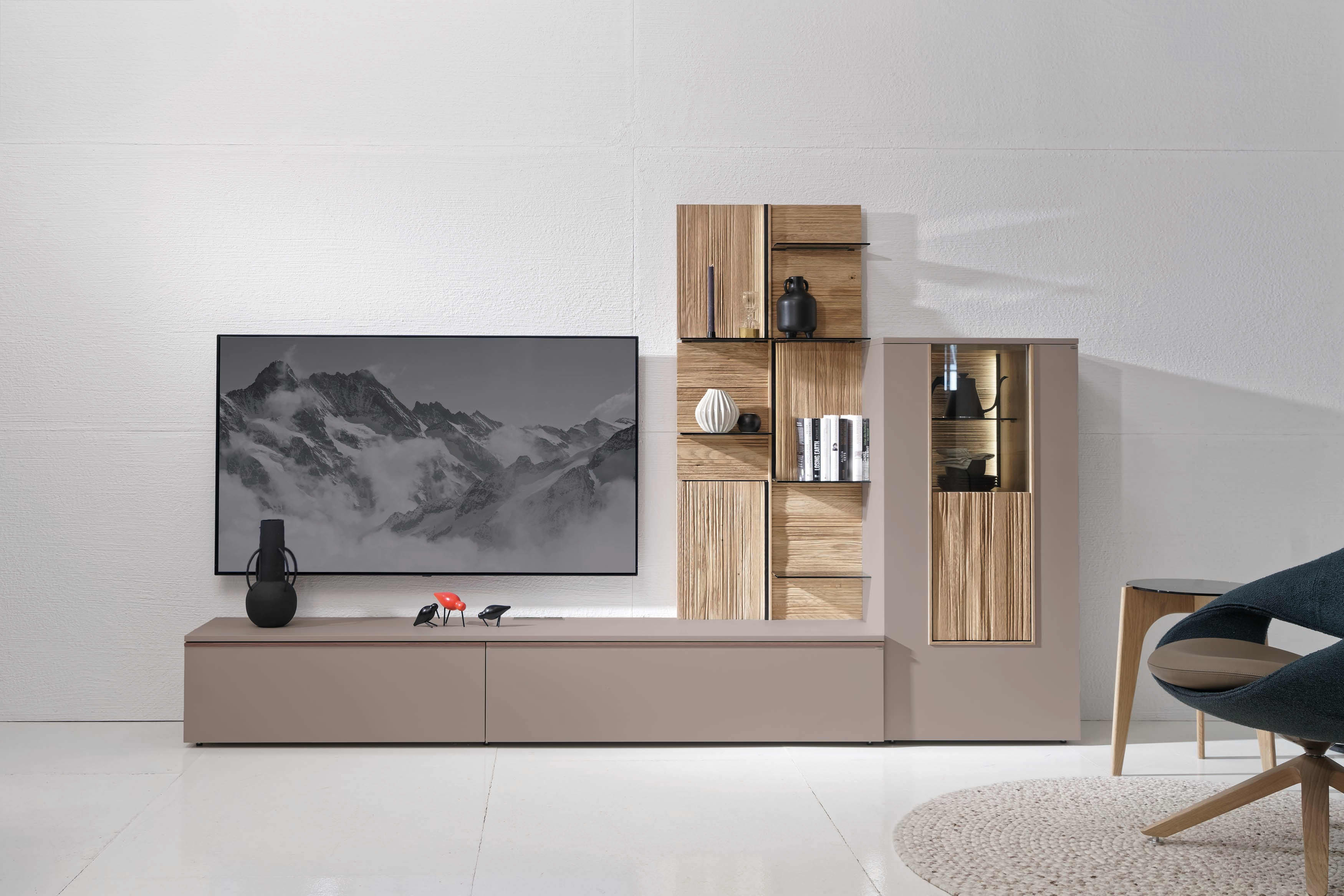 Modernes Wohnzimmer mit dem Voglauer Wohnmöbel Lacera: ein schlichter Schrank mit einem an der Wand befestigten Fernseher, stilvollen Regalen, Büchern und dekorativen Vasen. Modernes Wohnzimmer mit dem Voglauer Wohnmöbel Lacera: ein schlichter Schrank mit einem an der Wand befestigten Fernseher, stilvollen Regalen, Büchern und dekorativen Vasen.