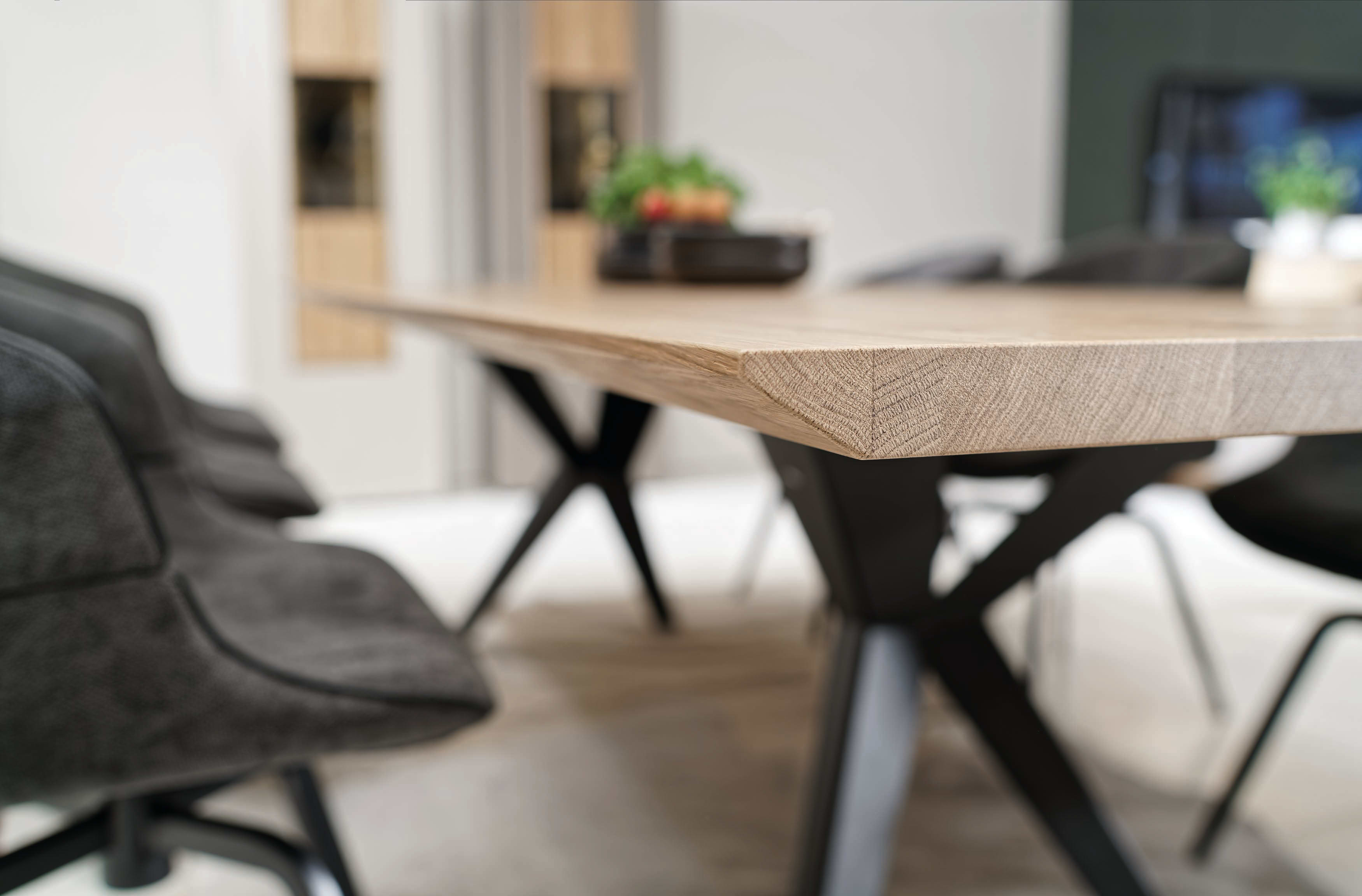 Nahaufnahme des Voglauer Esstisch Lacera, eines modernen Holztisches, der von schwarzen Stühlen umgeben ist und in dessen Mitte eine kleine Pflanze steht. Nahaufnahme des Voglauer Esstisch Lacera, eines modernen Holztisches, der von schwarzen Stühlen umgeben ist und in dessen Mitte eine kleine Pflanze steht.