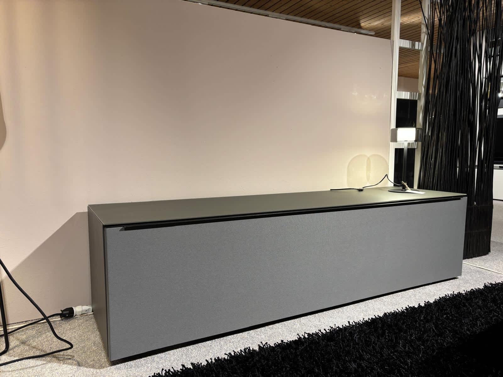 Das Spectral Lowboard Bravo, ein moderner grauer Schrank mit schwarzer Platte, steht vor einer hellen Wand und wird von einer kleinen Lampe zu seiner Rechten beleuchtet. Das Spectral Lowboard Bravo, ein moderner grauer Schrank mit schwarzer Platte, steht vor einer hellen Wand und wird von einer kleinen Lampe zu seiner Rechten beleuchtet.