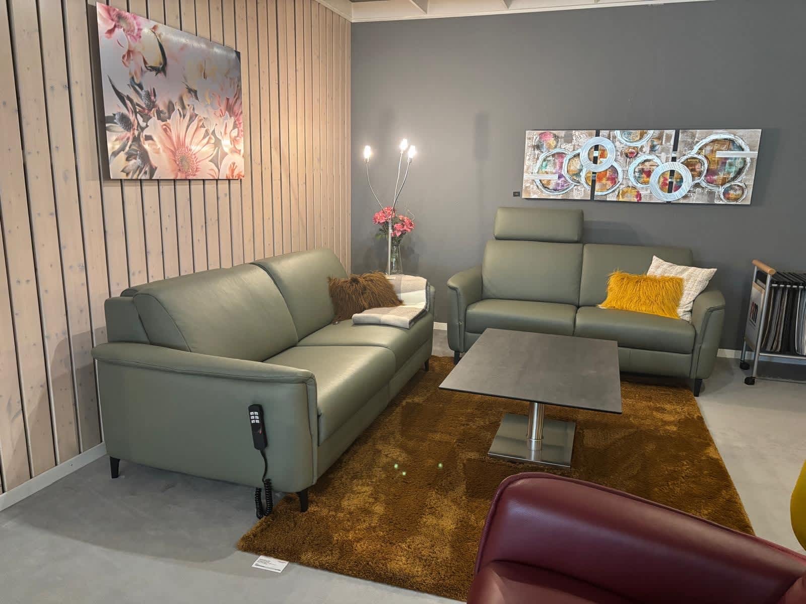 Ein modernes Wohnzimmer mit den grünen Sofas der PM Oelsa Polstergruppe „Ravenna“, einem braunen Teppich, Wandbildern und einer Stehlampe in einer gemütlichen, gut beleuchteten Ecke. Ein modernes Wohnzimmer mit den grünen Sofas der PM Oelsa Polstergruppe „Ravenna“, einem braunen Teppich, Wandbildern und einer Stehlampe in einer gemütlichen, gut beleuchteten Ecke.
