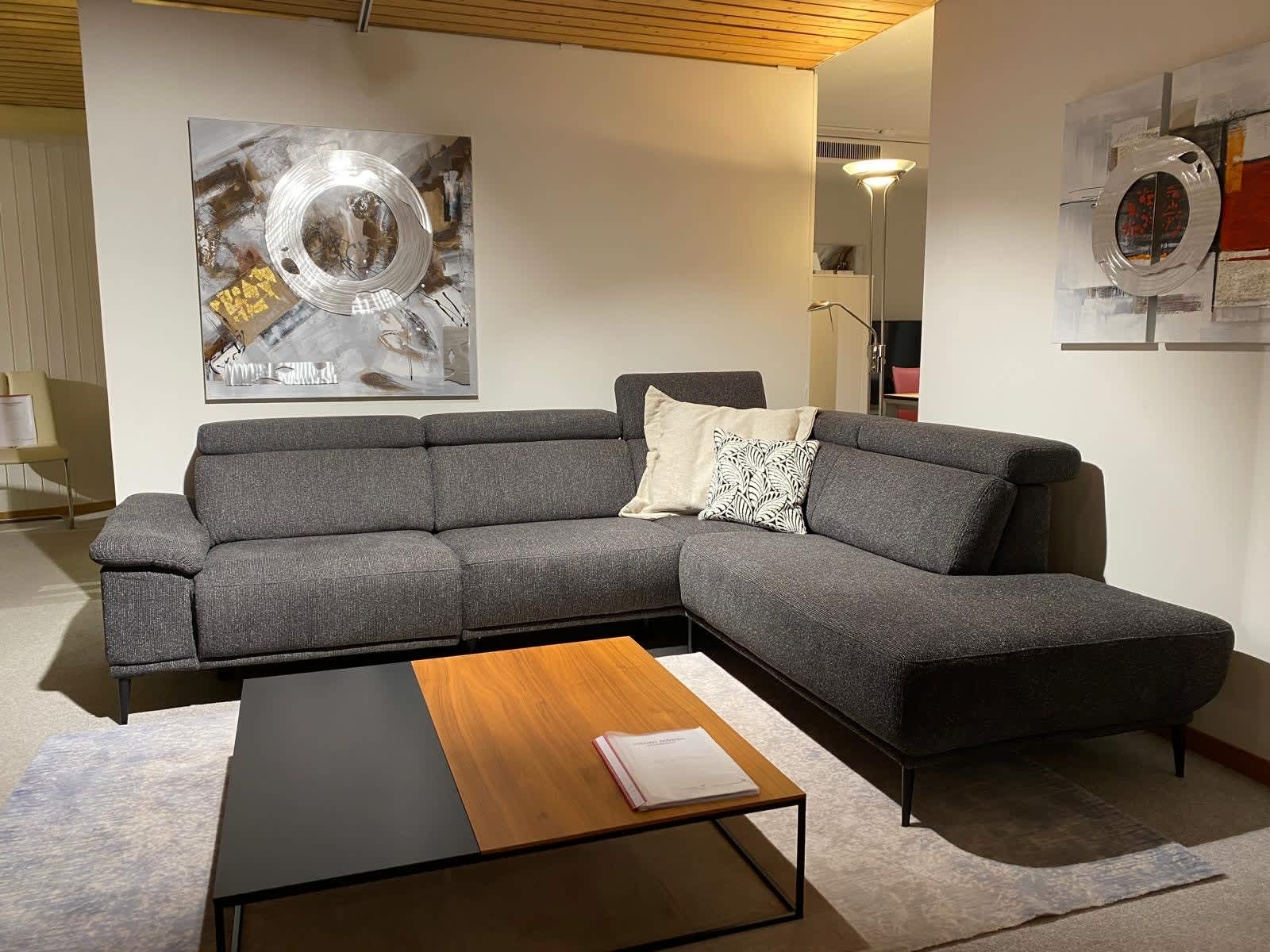 Ein modernes Wohnzimmer mit dem Sofa „Moon“ von Dietsch in Dunkelgrau, einem Couchtisch aus Holz und abstrakten Kunstwerken an den Wänden. Ein modernes Wohnzimmer mit dem Sofa „Moon“ von Dietsch in Dunkelgrau, einem Couchtisch aus Holz und abstrakten Kunstwerken an den Wänden.