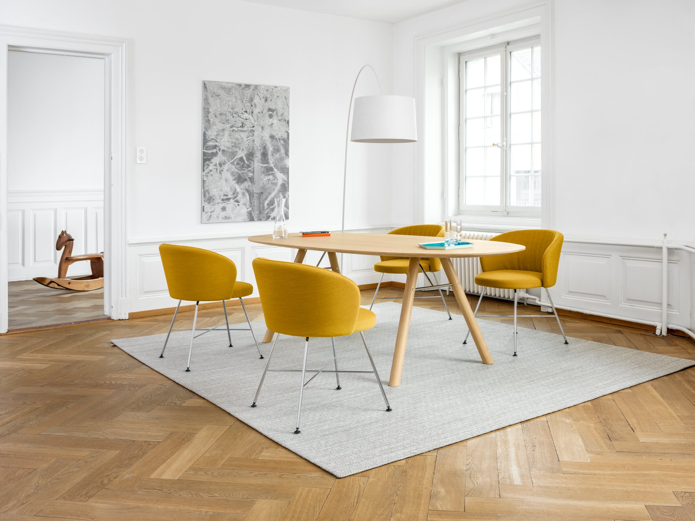 Ein modernes Esszimmer mit gelben Stühlen, dem Holztisch „Akio Oval“ von Girsberger, einer Stehlampe und Sonnenlicht, das durch das Fenster hereinströmt. Ein modernes Esszimmer mit gelben Stühlen, dem Holztisch „Akio Oval“ von Girsberger, einer Stehlampe und Sonnenlicht, das durch das Fenster hereinströmt.