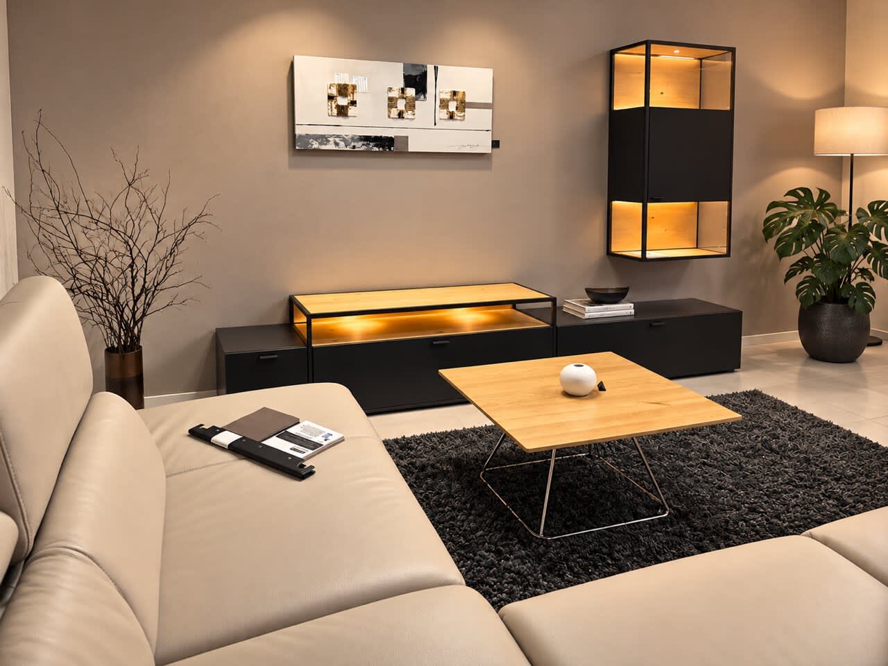 Modernes Wohnzimmer mit der beleuchteten Wohnwand „Plan X6“ von Venjakob, ergänzt durch ein beiges Sofa, einen Couchtisch aus Holz und einen schwarzen Teppich. Modernes Wohnzimmer mit der beleuchteten Wohnwand „Plan X6“ von Venjakob, ergänzt durch ein beiges Sofa, einen Couchtisch aus Holz und einen schwarzen Teppich.