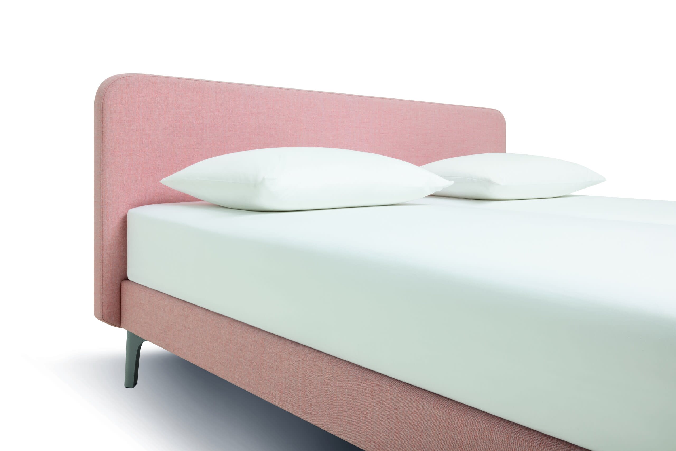 Das Riposa Boxspringbett Slow hat ein minimalistisches Design mit einem rosa gepolsterten Kopfteil, einer weißen Matratze und zwei weißen Kissen auf weißem Grund.
