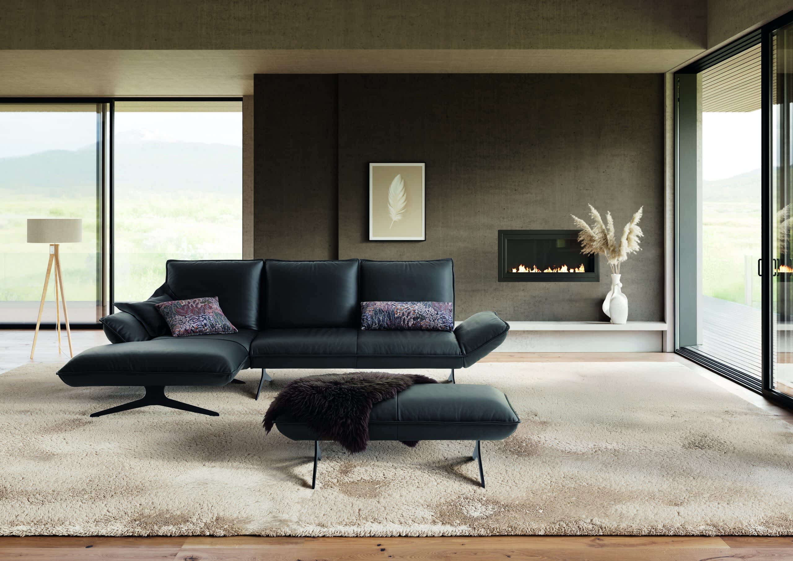 Modernes Wohnzimmer mit dem Koinor Sofa Buddy in Schwarz, kombiniert mit einer Ottomane, einem Kamin, einer Stehlampe und großen Fenstern, die einen Ausblick auf die Landschaft bieten. Modernes Wohnzimmer mit dem Koinor Sofa Buddy in Schwarz, kombiniert mit einer Ottomane, einem Kamin, einer Stehlampe und großen Fenstern, die einen Ausblick auf die Landschaft bieten.