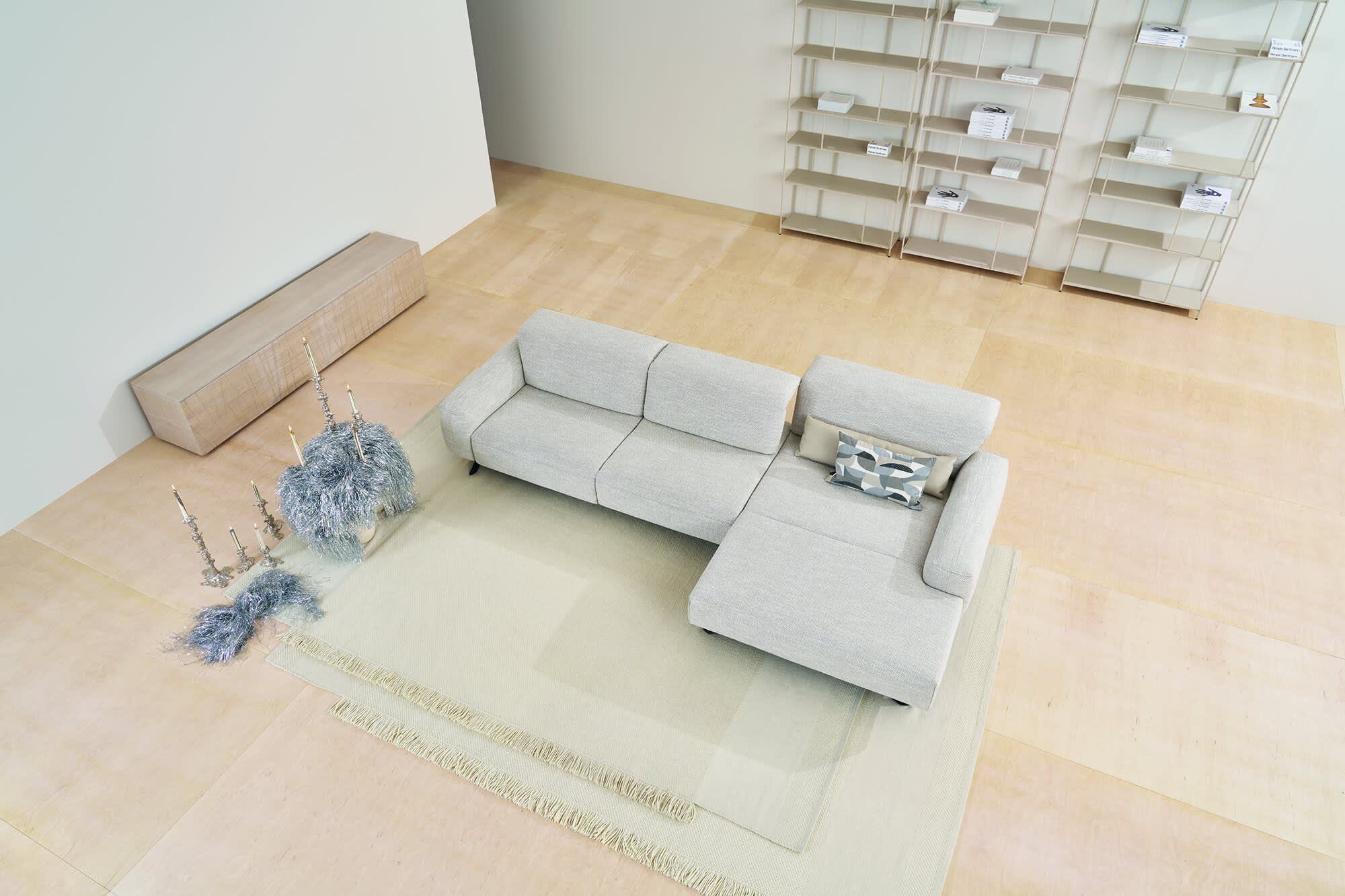 Modernes Wohnzimmer mit dem Himolla Sofa Signa 1552 in Hellgrau, gepaart mit Teppichen, minimalem Dekor und leeren Regalen. Modernes Wohnzimmer mit dem Himolla Sofa Signa 1552 in Hellgrau, gepaart mit Teppichen, minimalem Dekor und leeren Regalen.