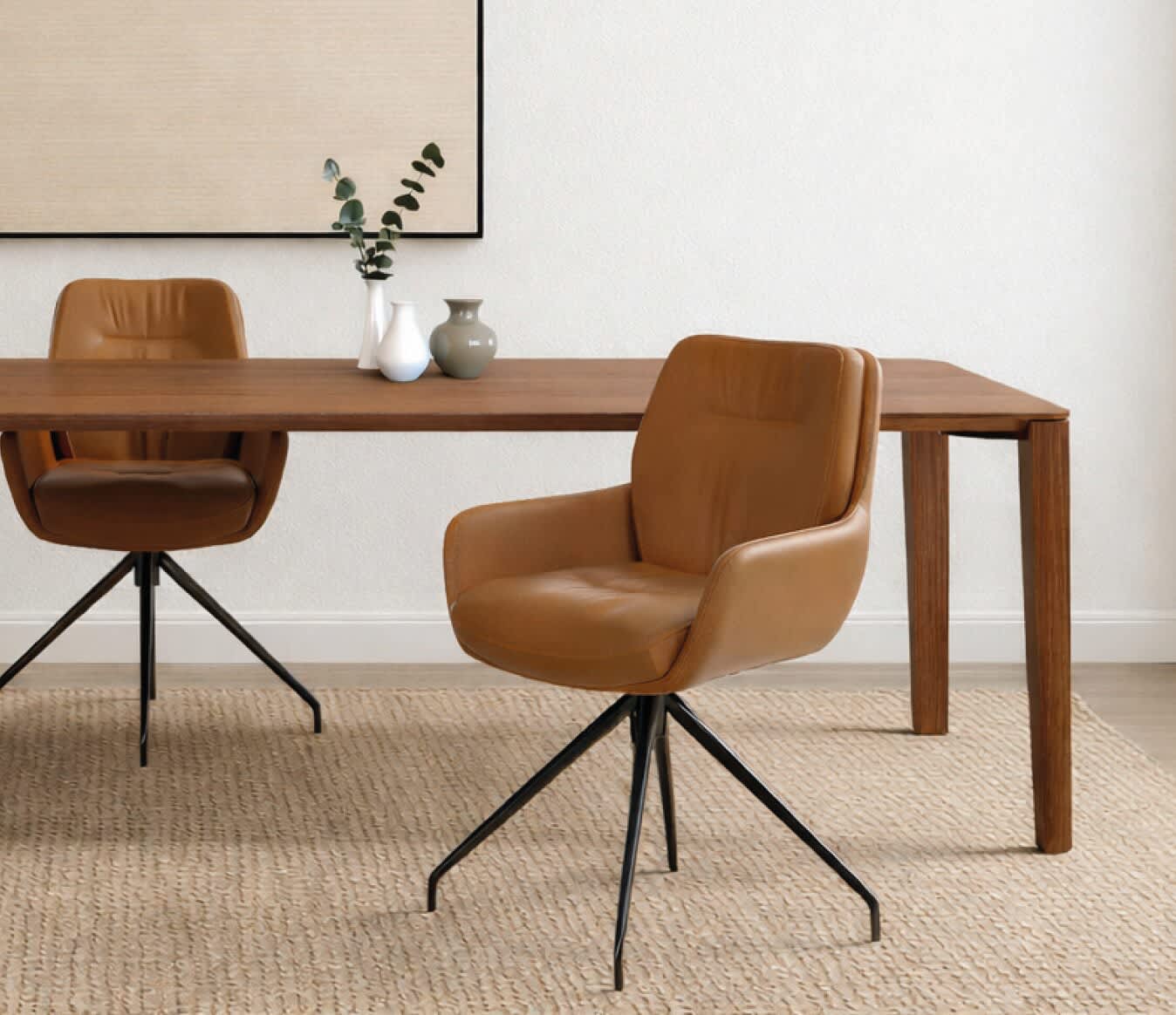 Espace à manger moderne avec deux chaises Sit Mobilia Enna, une table en bois, des vases décoratifs, une œuvre murale neutre et un tapis tissé. Espace à manger moderne avec deux chaises Sit Mobilia Enna, une table en bois, des vases décoratifs, une œuvre murale neutre et un tapis tissé.
