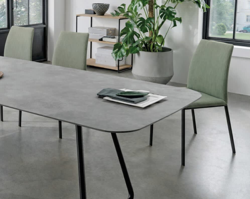 Modernes Esszimmer mit einem grauen Tisch, Sit Mobilia Stuhl Fedora grün, einer Topfpflanze und einem Regal mit Büchern am Fenster. Modernes Esszimmer mit einem grauen Tisch, Sit Mobilia Stuhl Fedora grün, einer Topfpflanze und einem Regal mit Büchern am Fenster.