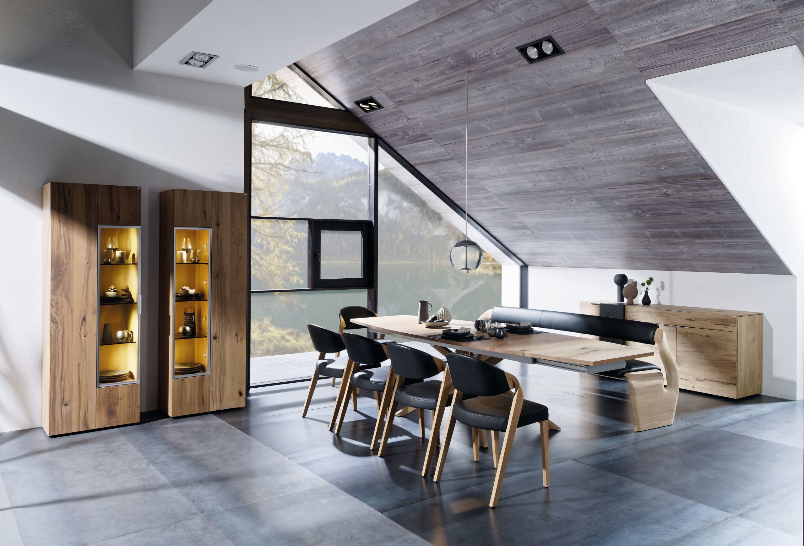 Modernes Esszimmer mit Holzmöbeln, Voglauer Stuhl 35 in Schwarz und großen Fenstern unter einer schrägen Decke. Modernes Esszimmer mit Holzmöbeln, Voglauer Stuhl 35 in Schwarz und großen Fenstern unter einer schrägen Decke.