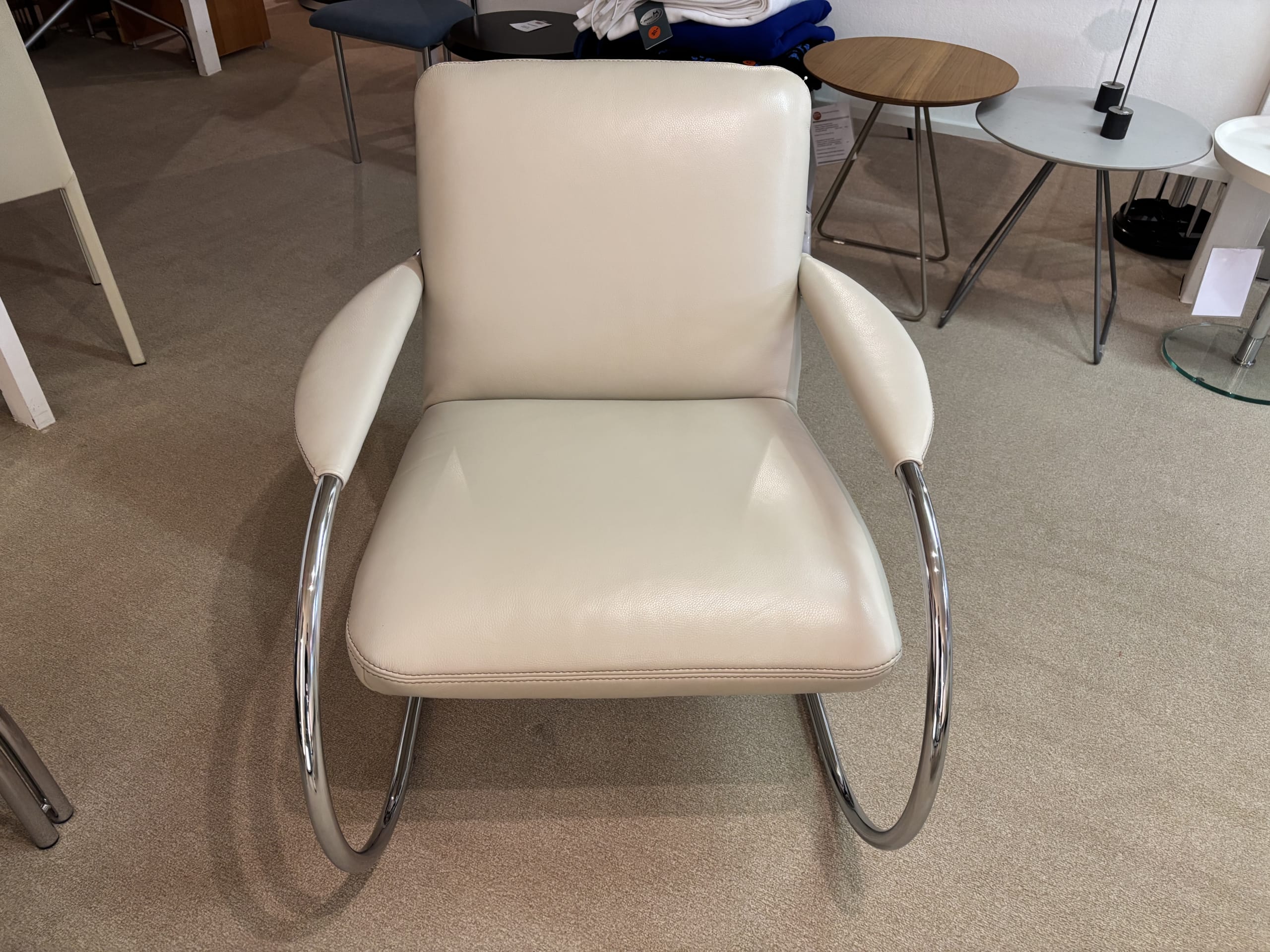 Die Polstergruppe Samiraa, ein weißer Sessel mit Chrombeinen, steht in einem Raum, umgeben von Beistelltischen.