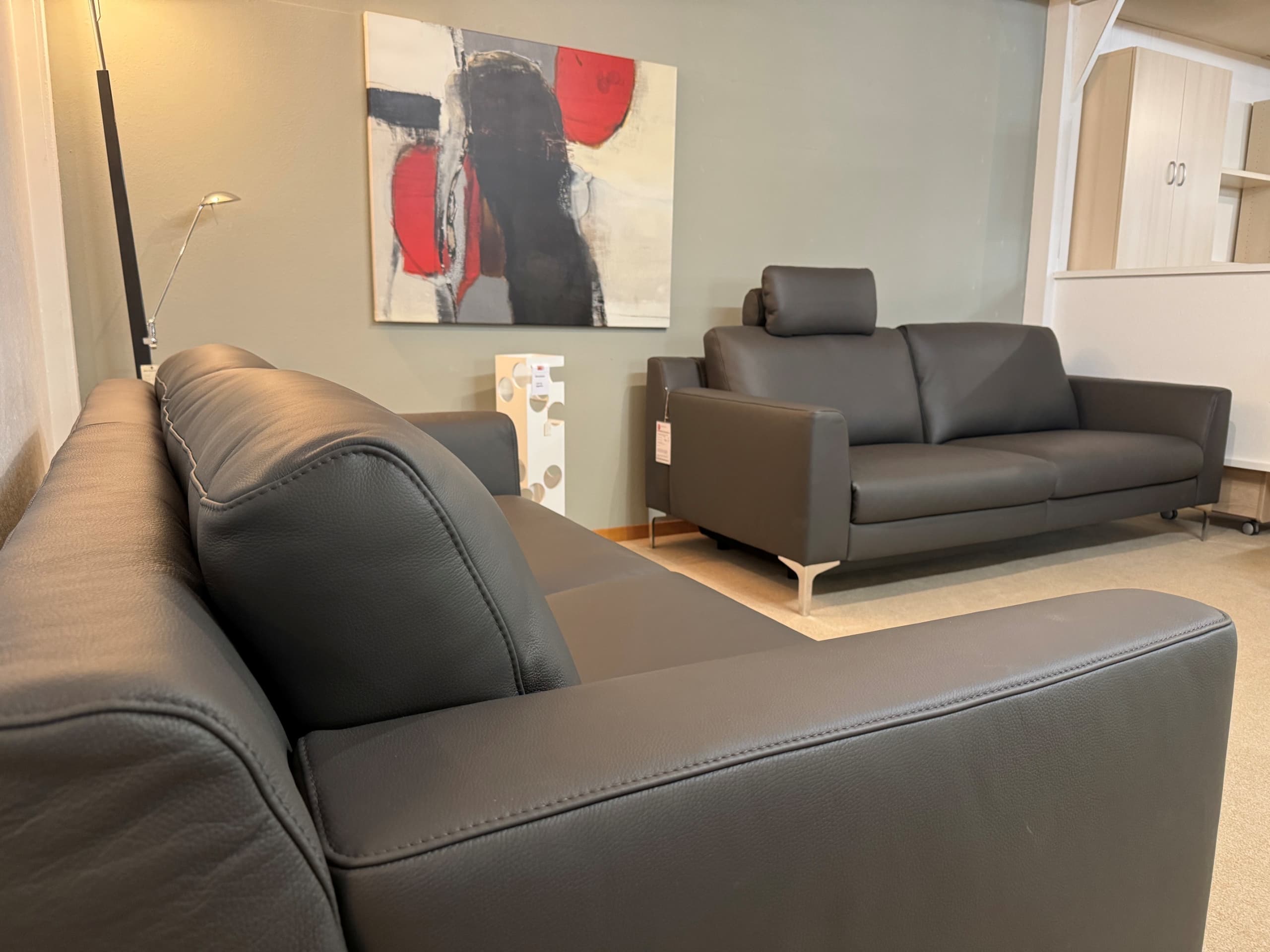 Deux canapés en cuir noir du groupe de canapés « Mesa » de DFM dans un salon moderne, complétés par de l'art abstrait et une lampe sur pied en arrière-plan.