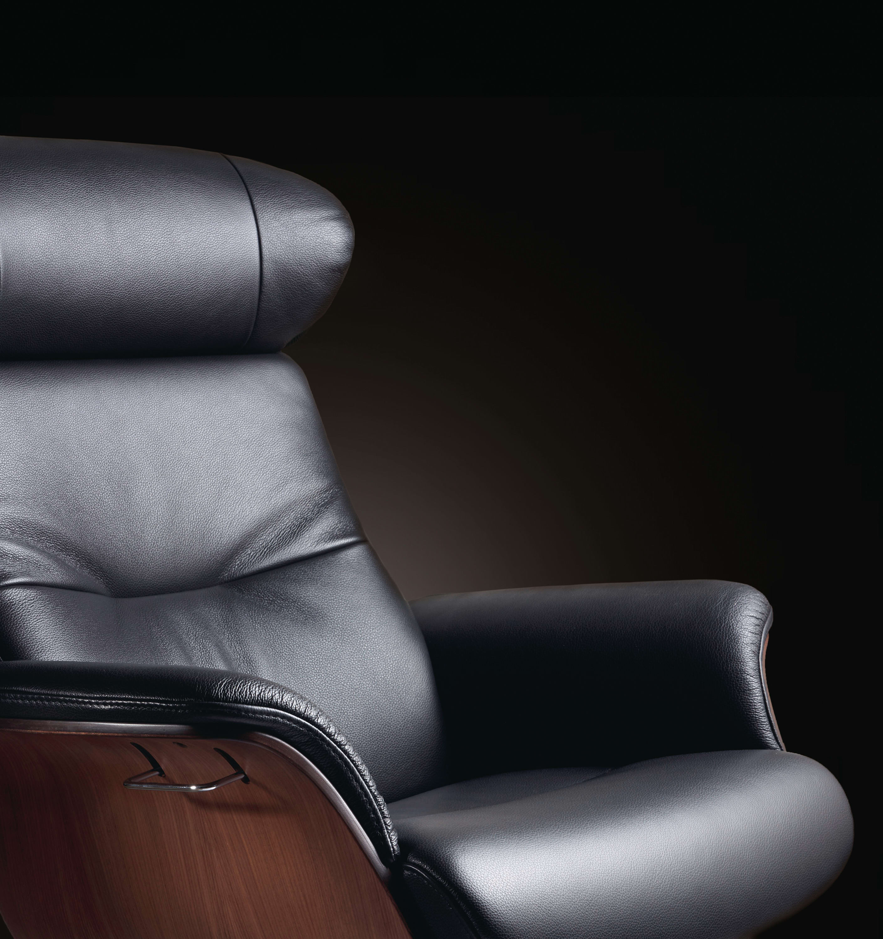 Fauteuil Time Out avec repose-pieds en cuir noir et accoudoirs en bois sur fond sombre.