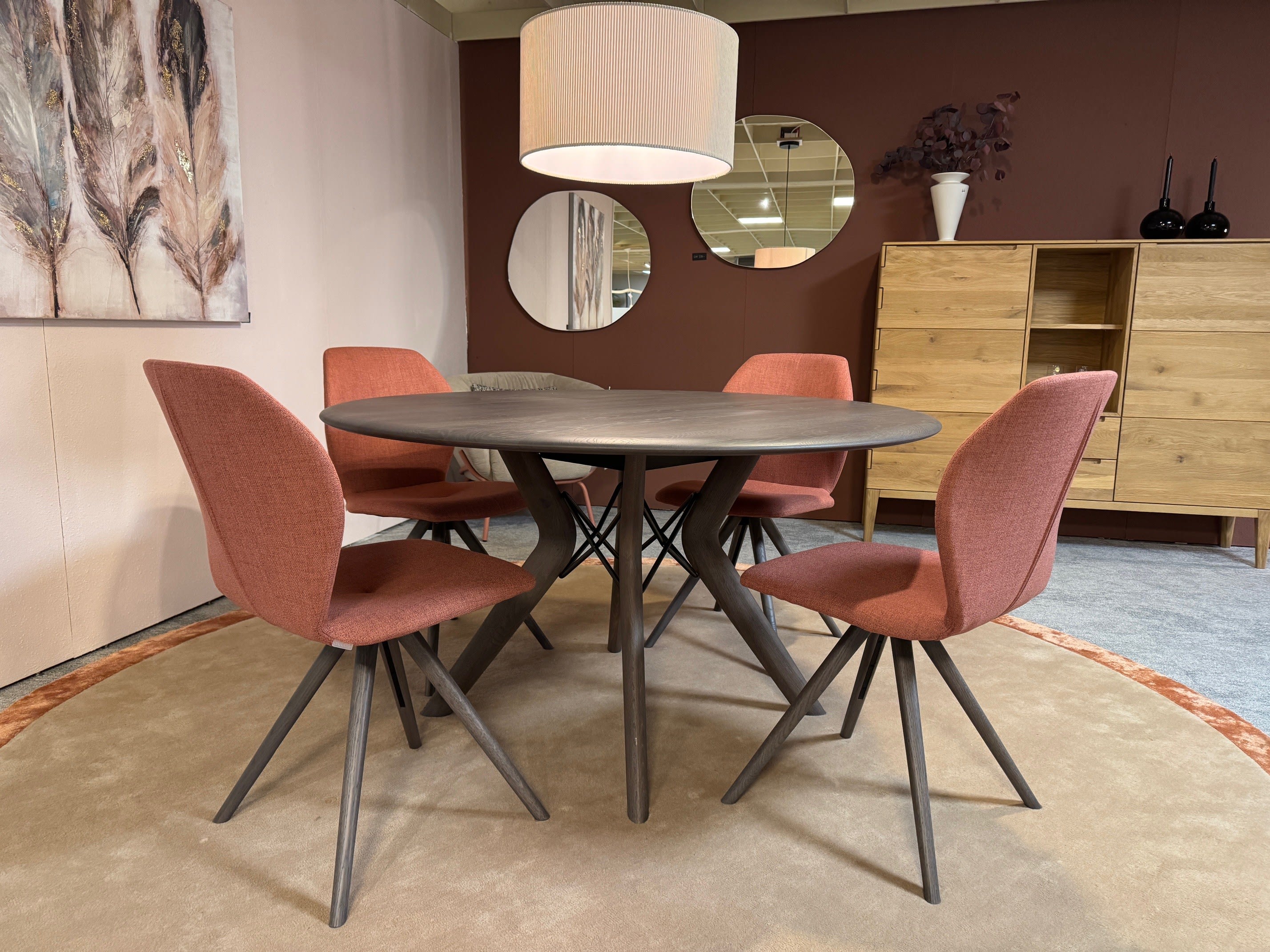 Runder Esstisch aus Holz mit vier Stühlen Mobitec Stuhl Mood 91, einer Hängeleuchte und moderner Dekoration in einem gemütlichen Raum. Runder Esstisch aus Holz mit vier Stühlen Mobitec Stuhl Mood 91, einer Hängeleuchte und moderner Dekoration in einem gemütlichen Raum.