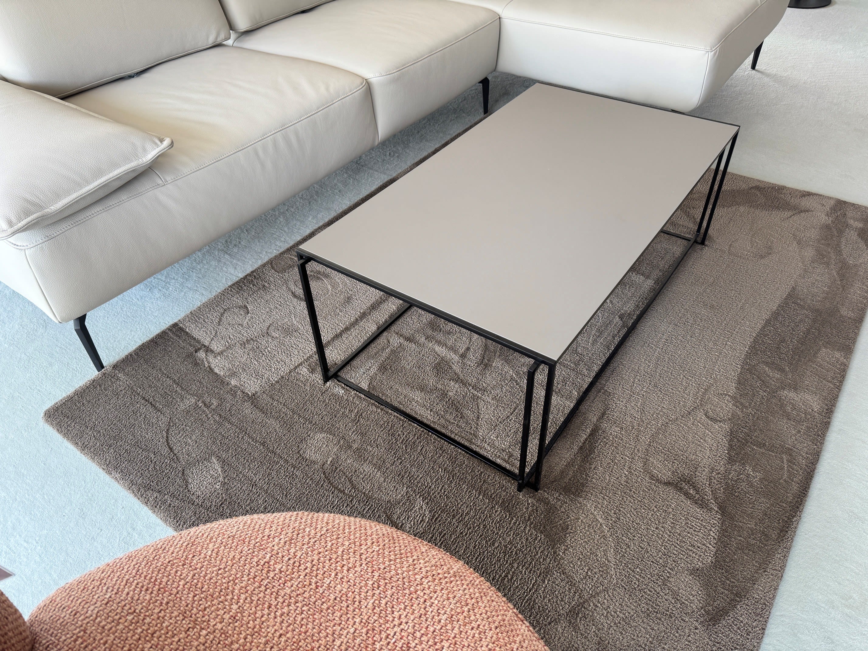 Der Bacher Couchtisch Minero steht auf einem strukturierten Teppich neben einem weißen Sofa und einem rosa Sessel in einem hellen Wohnzimmer.