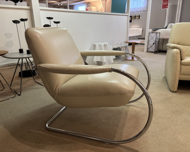 Dans une salle d&#39;exposition, le groupe de rembourrage Samiraa présente un fauteuil moderne en cuir beige avec des accoudoirs courbés et des pieds en métal.