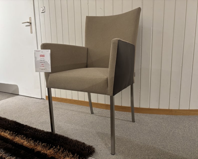 Ein grauer Stoffsessel mit Metallrahmen von Büromöbel mit 3 Boxen Window steht neben einer weißen Tür auf einem grauen Teppich, begleitet von einem braun gestreiften Läufer.
