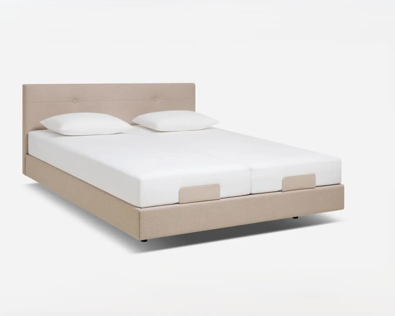 Beige gepolstertes Kingsize-Bett mit Riposa Matratze Superspring TEX forte, einfachem Kopfteil und zwei weißen Kissen auf weißem Hintergrund.