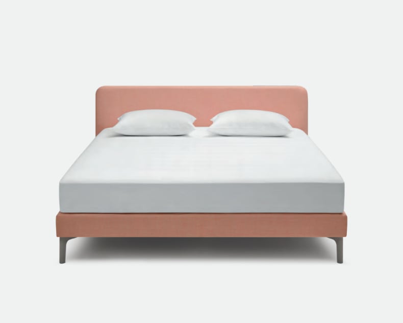 Das Riposa Boxspringbett Slow ist ein modernes Bett mit einem rosa gepolsterten Kopf- und Unterteil, ergänzt durch zwei weiße Kissen und eine makellos weiße Matratze.