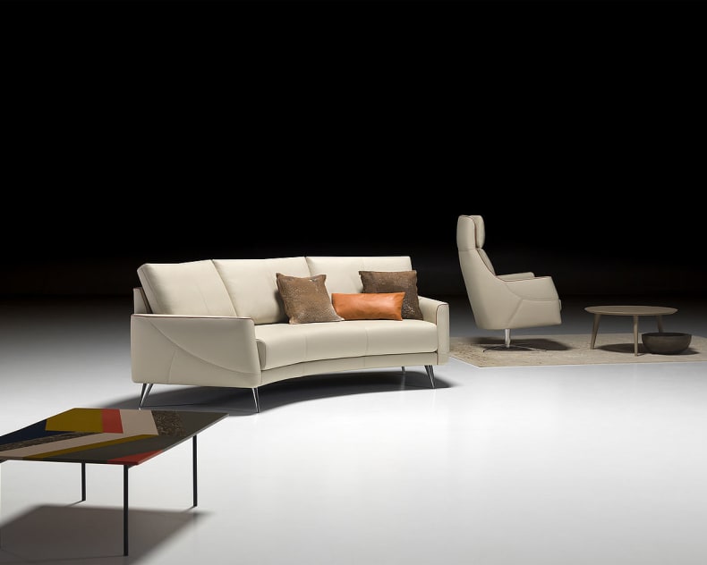Modernes Wohnzimmer mit dem Sofa Thalia 9182 in Creme, ergänzt durch einen Sessel, einen Couchtisch und Akzentkissen auf einem weißen Boden.