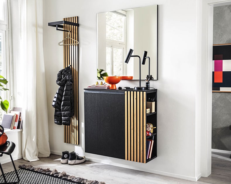 Moderner Eingangsbereich mit der Garderobe Punta in Schwarz und Holz, ergänzt durch einen Spiegel, einen Garderobenständer, Pflanzen und bunte dekorative Akzente.