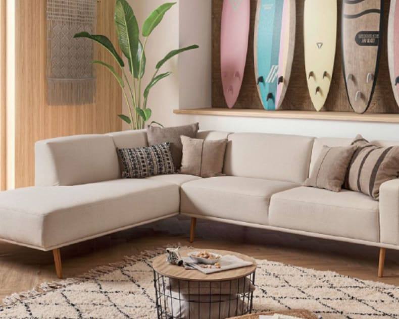 Das Sektionssofa Michigan der Polstergruppe steht in einem Wohnzimmer, das mit Surfbrettern, üppigen Pflanzen und küstennahen Akzenten eingerichtet ist.