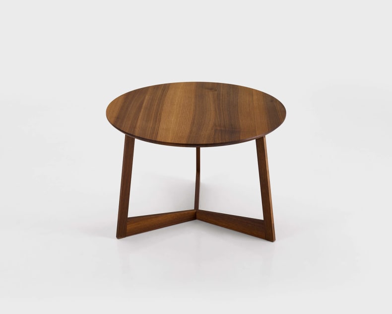Table ronde en bois à trois pieds inclinés et au design minimaliste sur fond blanc.