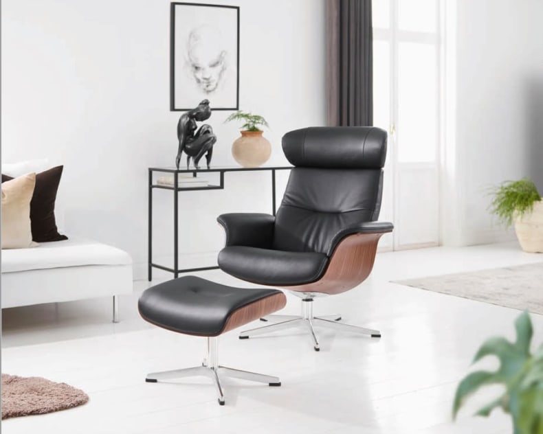 Un fauteuil Time Out avec son repose-pieds assorti, de couleur noire moderne, est placé dans un salon lumineux et minimaliste.